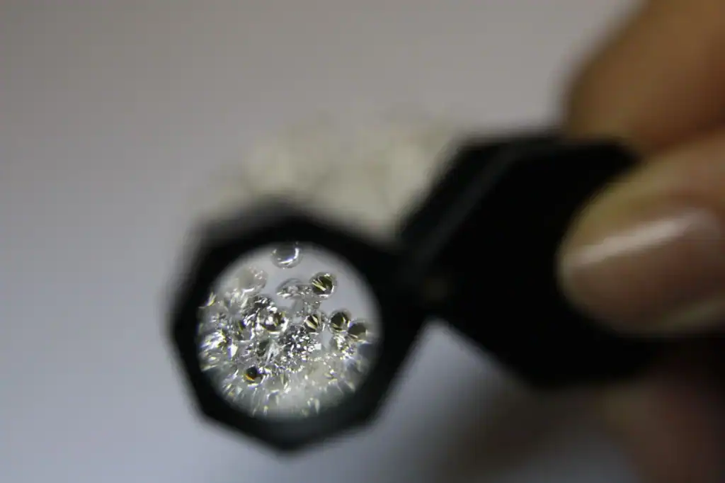 A jeweler holds a loupe over a group of small loose diamonds on the workbench.