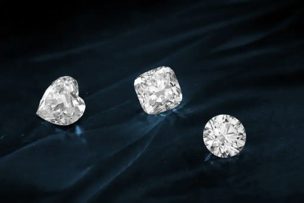 Three loose diamonds, a heart shape, a cushion cut and a round brilliant, on dark fabric.