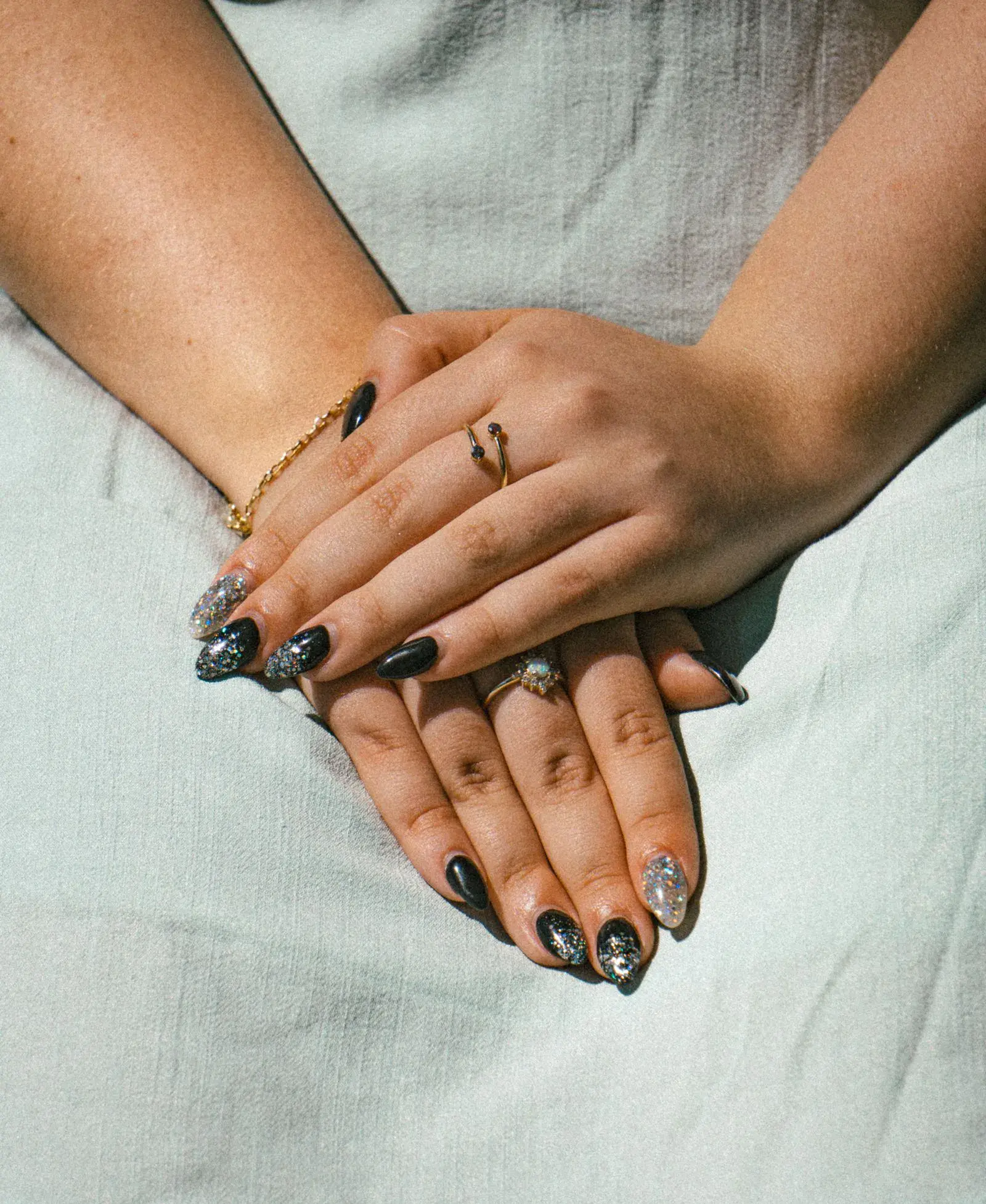 Two hands folded with short black almond nails with silver details and rings