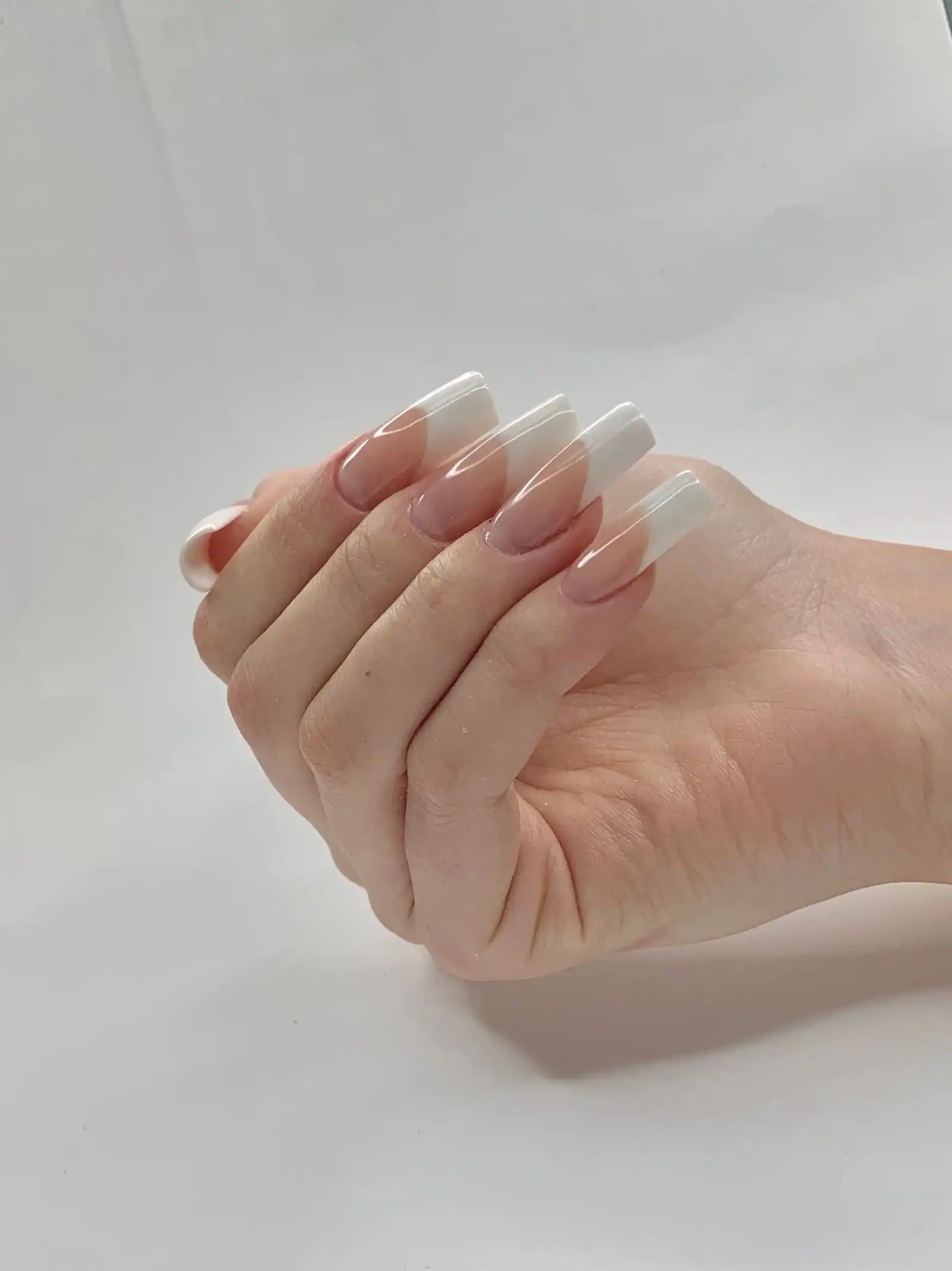 A hand with long French tip nails against a white background