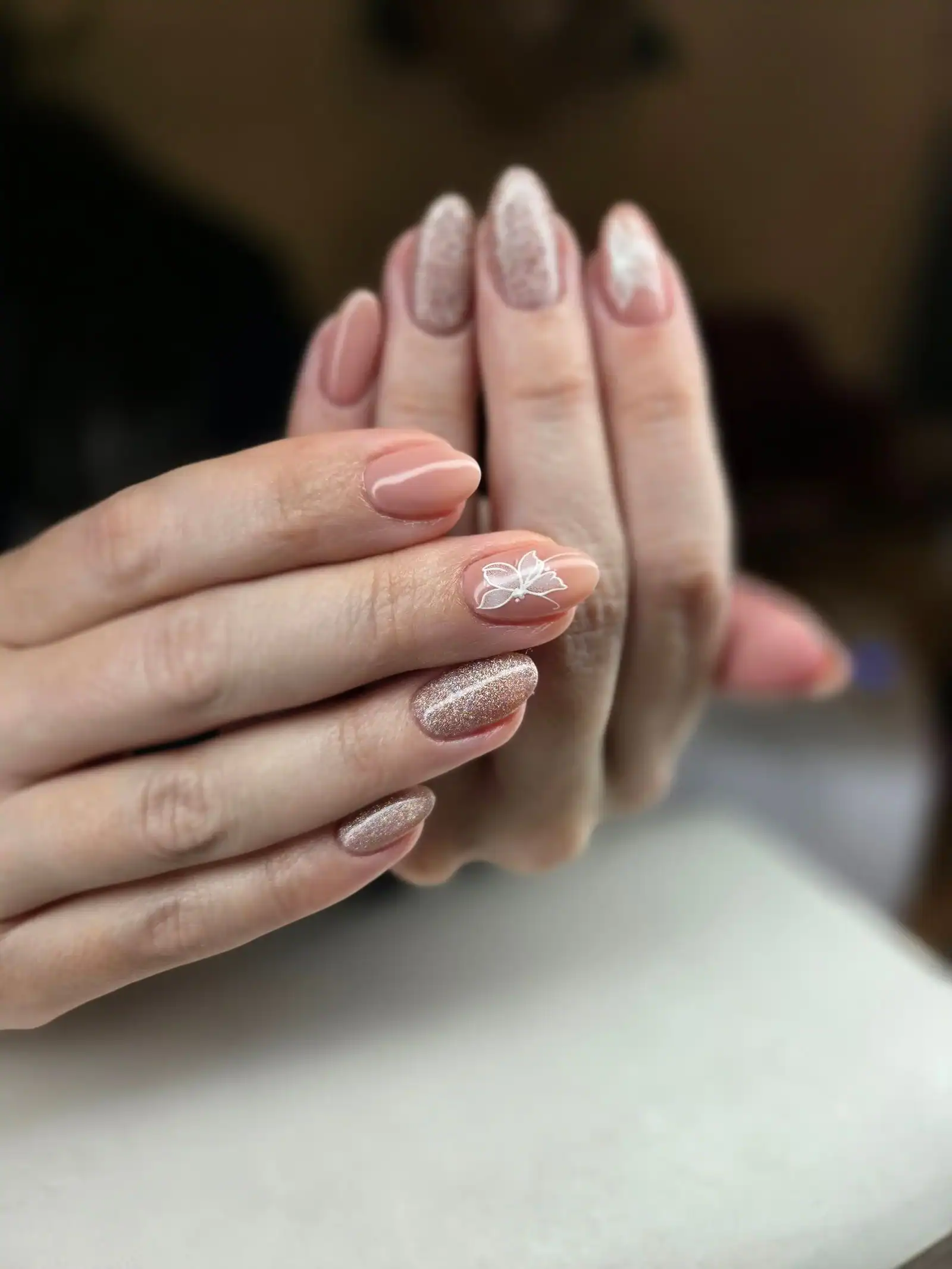 Two hands with nude almond nails, one with a glitter finish and one with a small bow design
