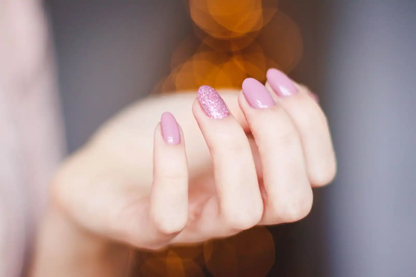 Baddie nail ideas: a hand with glossy pink almond nails and one glitter accent nail