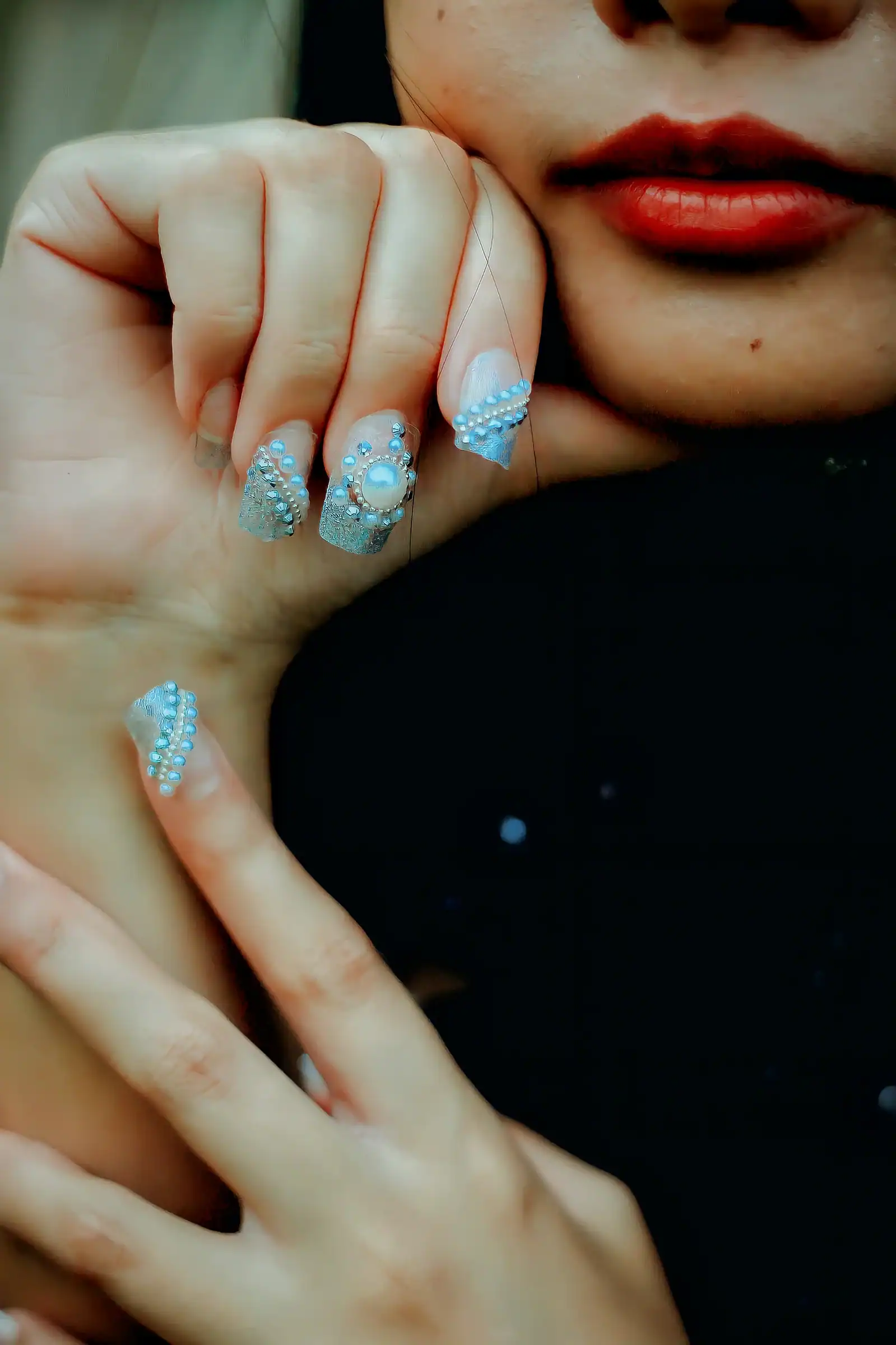 A hand near a face with light blue nail art and glitter