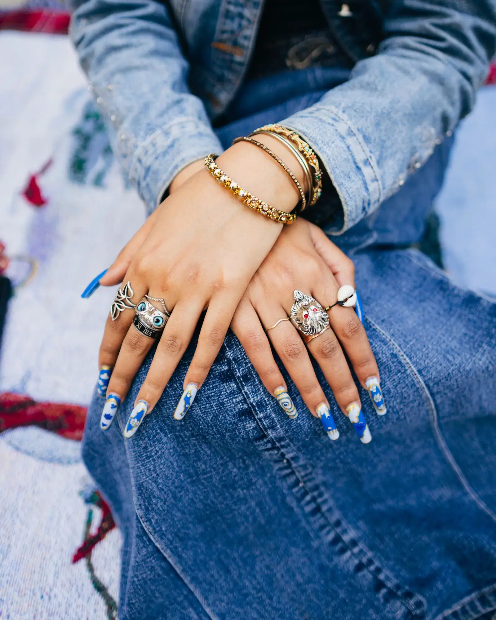 Hands with long light blue tipped nails resting on a denim jacket and jeans