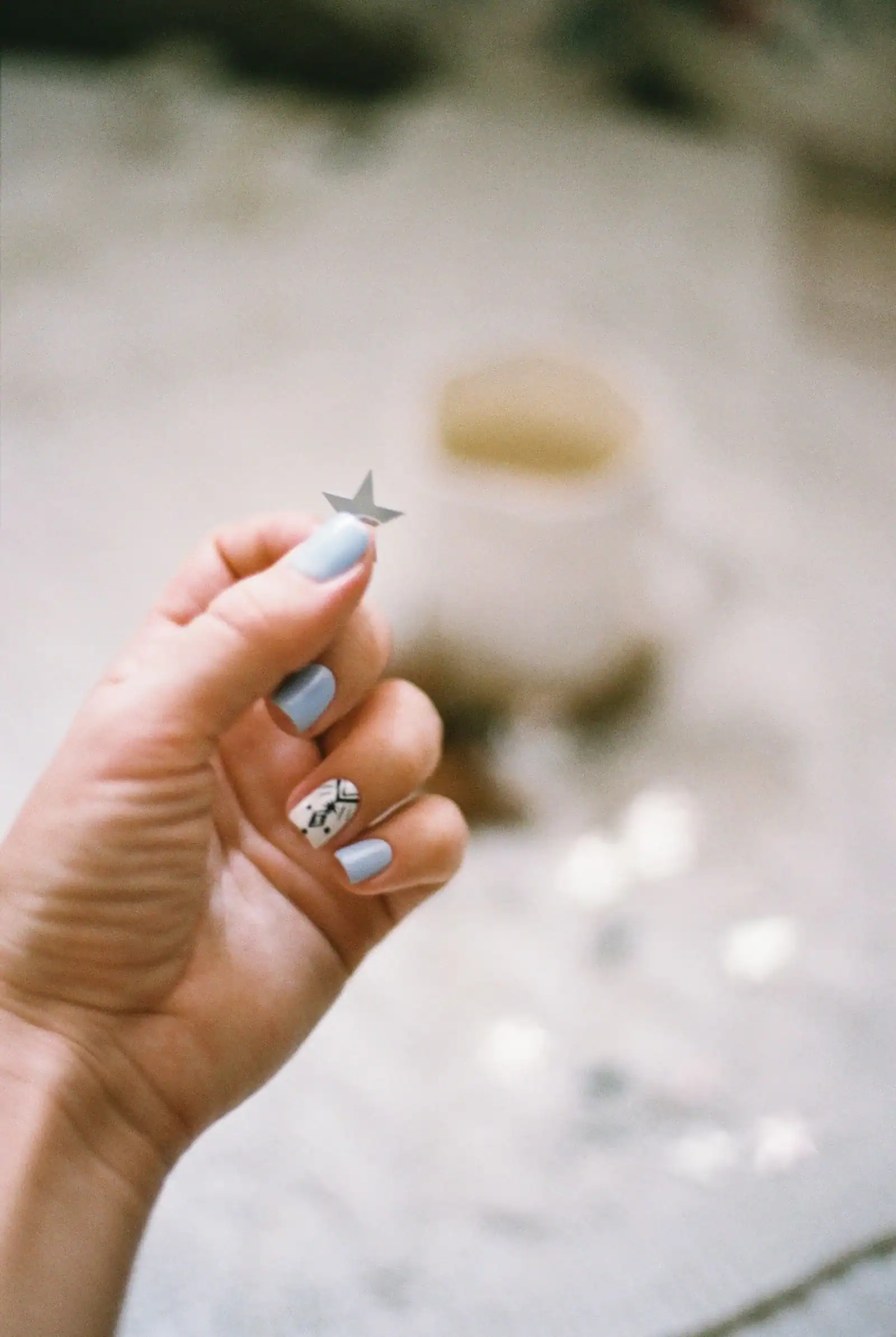 A hand with icy blue nails holding a small star ornament