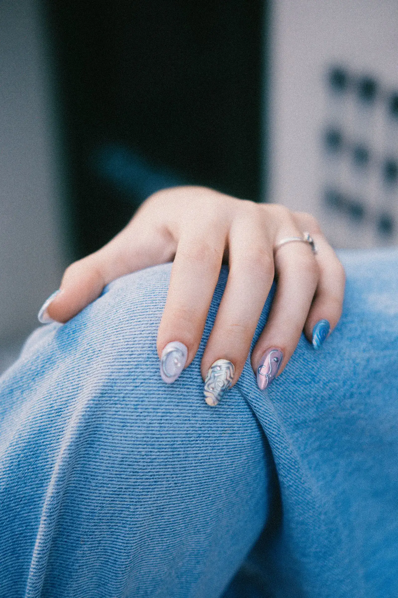A hand with pale blue glossy nails resting on a blue sweater