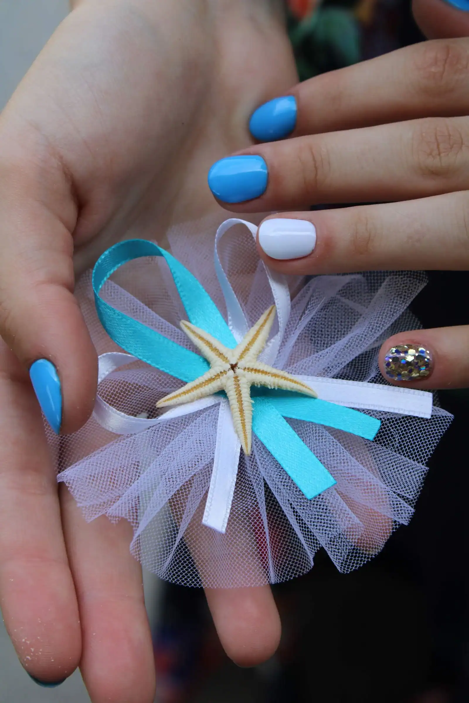 A hand with bright blue and white nails holding a starfish decoration
