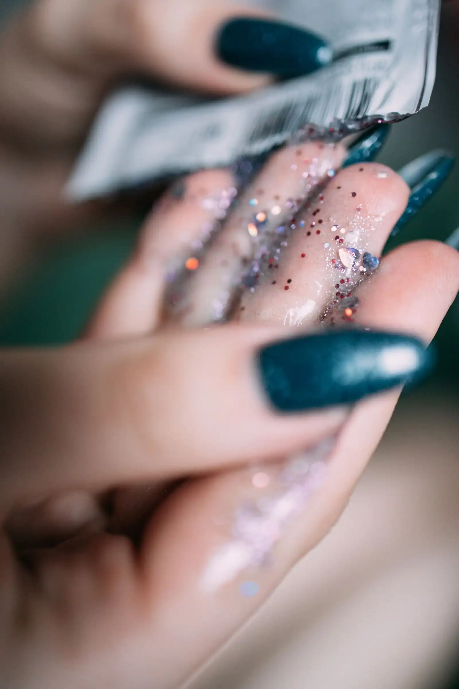 Teal and glittery nails being painted by hand