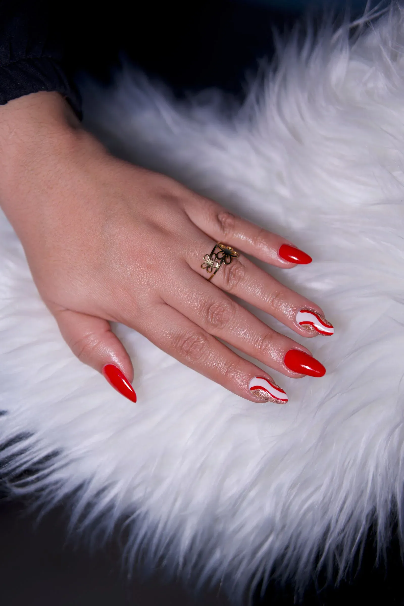 Almond nails in glossy red with curved red and white candy cane swirls, resting on white faux fur