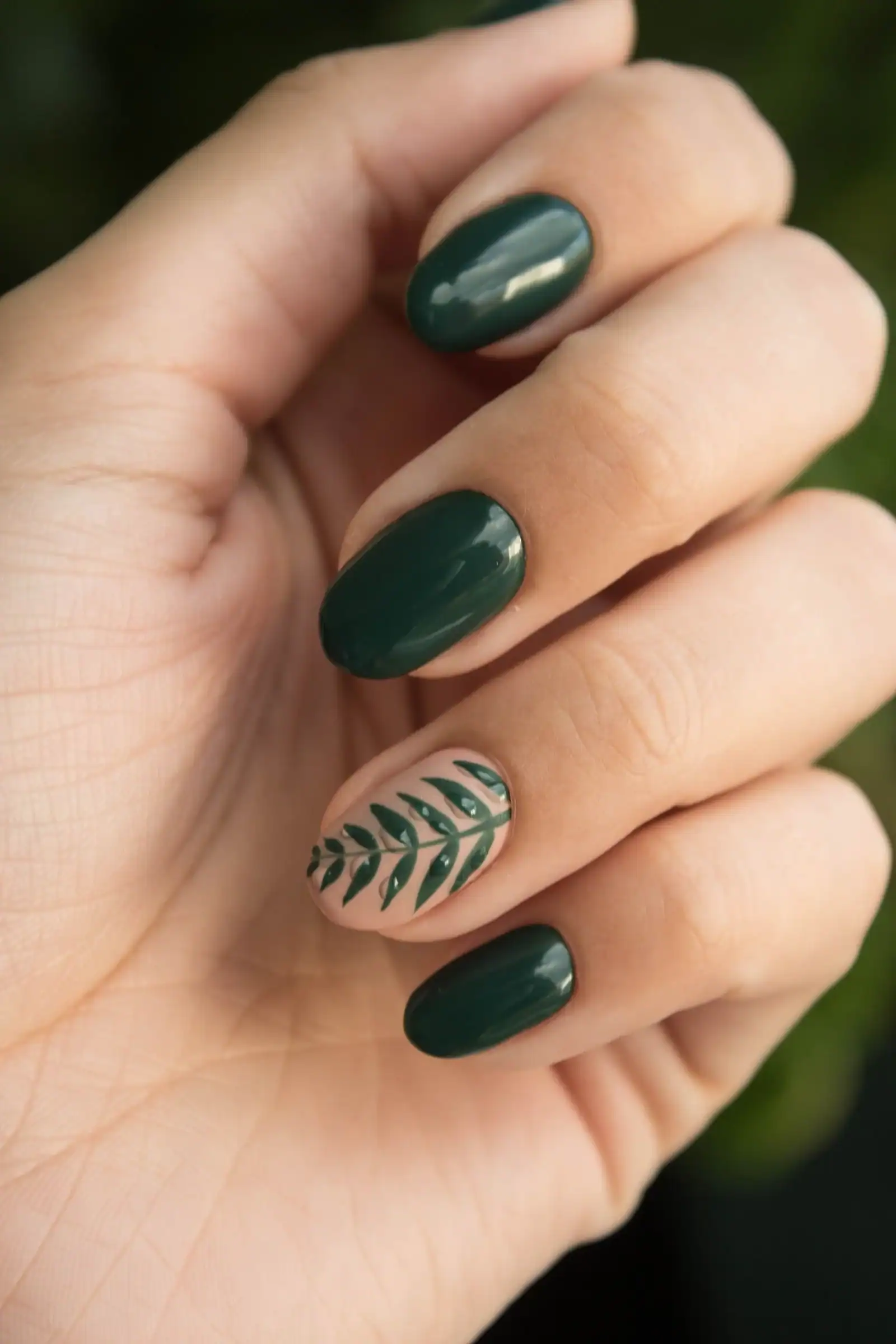 Glossy dark green nails with a painted green leaf design on one nail
