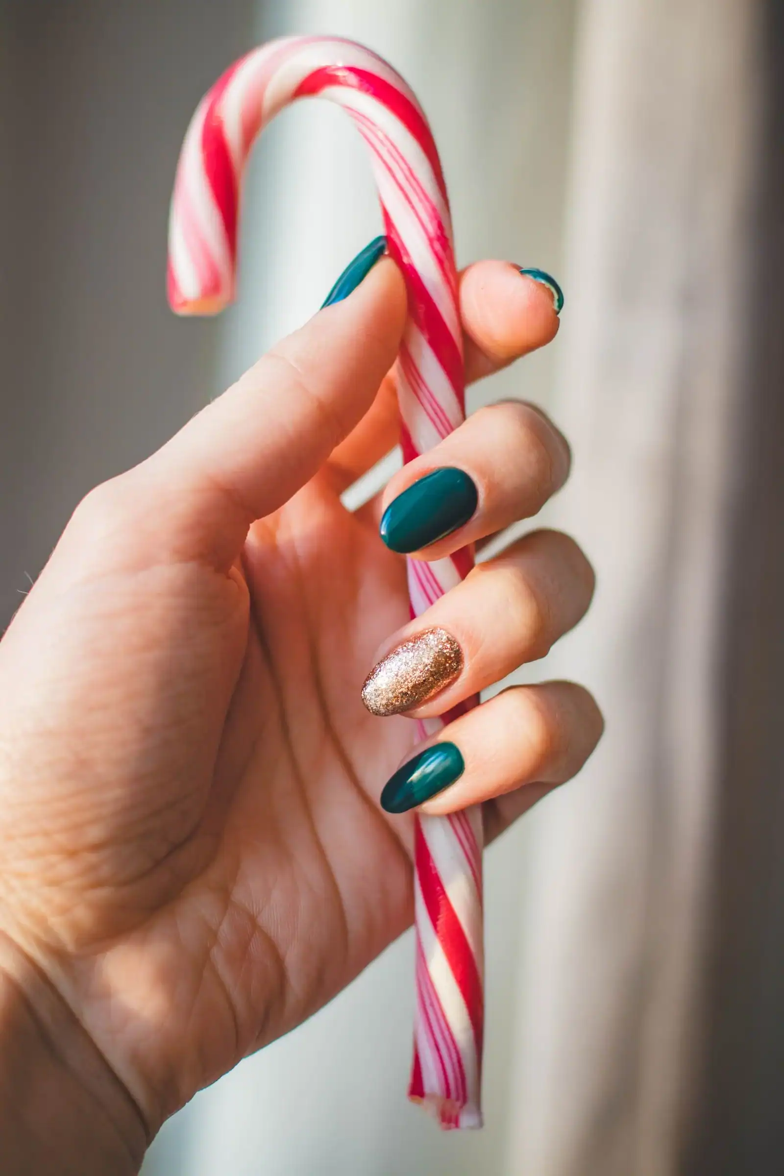 Forest green nails with one gold glitter nail, holding a red and white candy cane