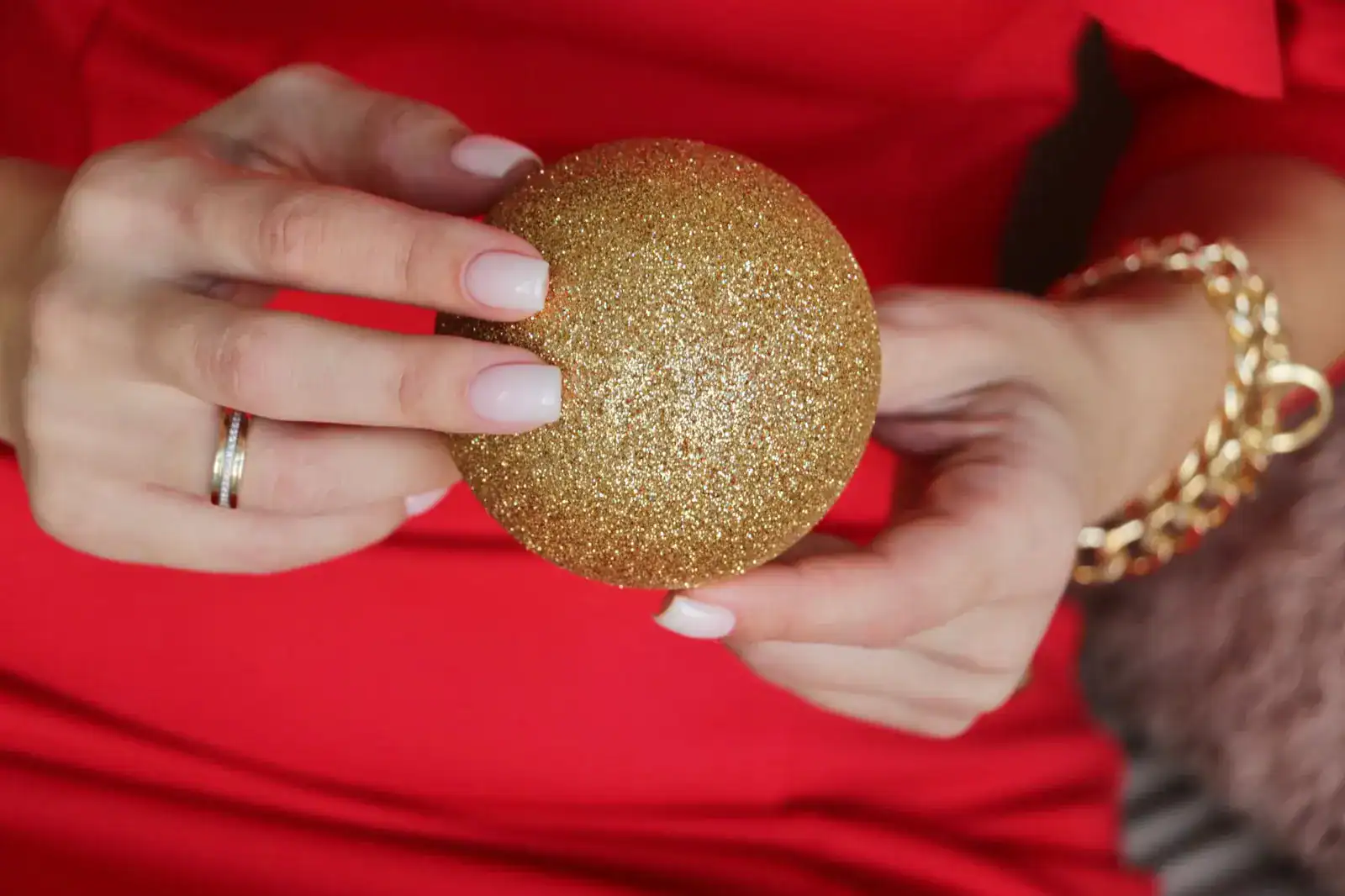 Milky pink nails holding a gold glitter ornament against red fabric