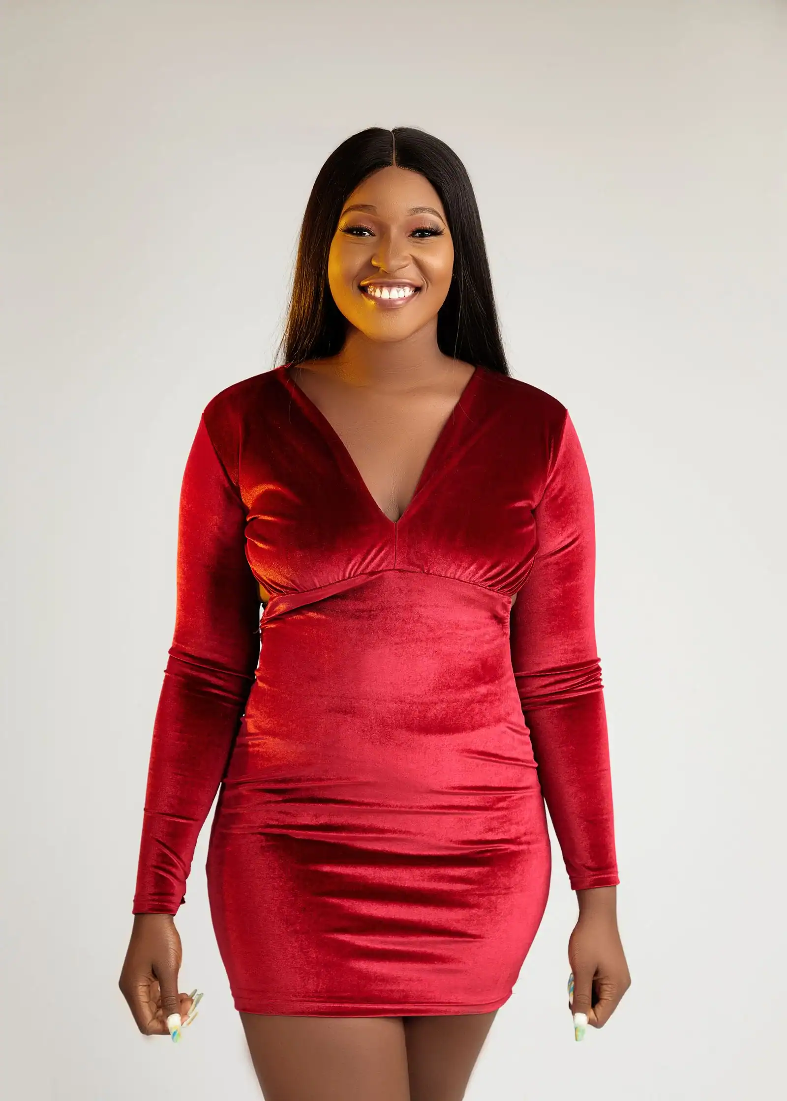 A smiling woman in a long-sleeve red velvet dress with a V-neck
