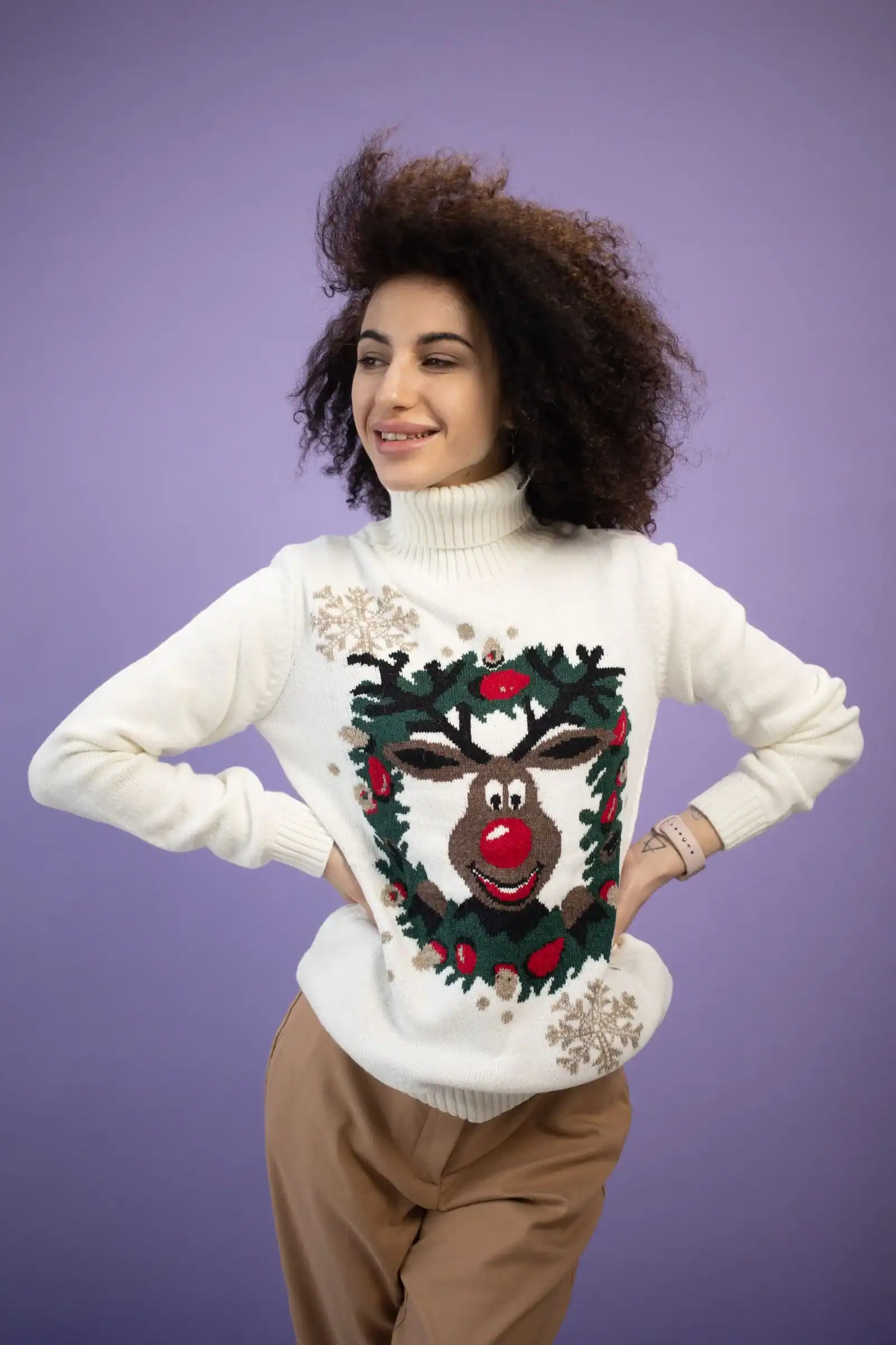 A smiling woman in a cream reindeer Christmas sweater and camel trousers