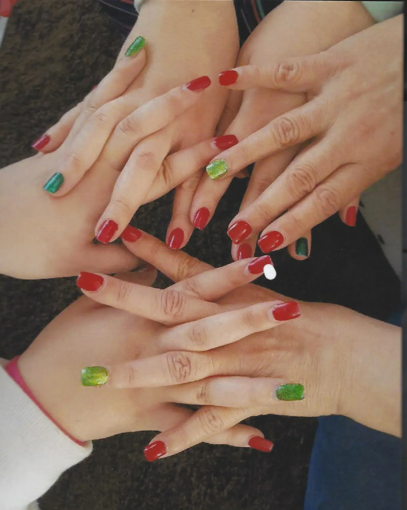 Several hands with red manicures and green accent nails stacked together