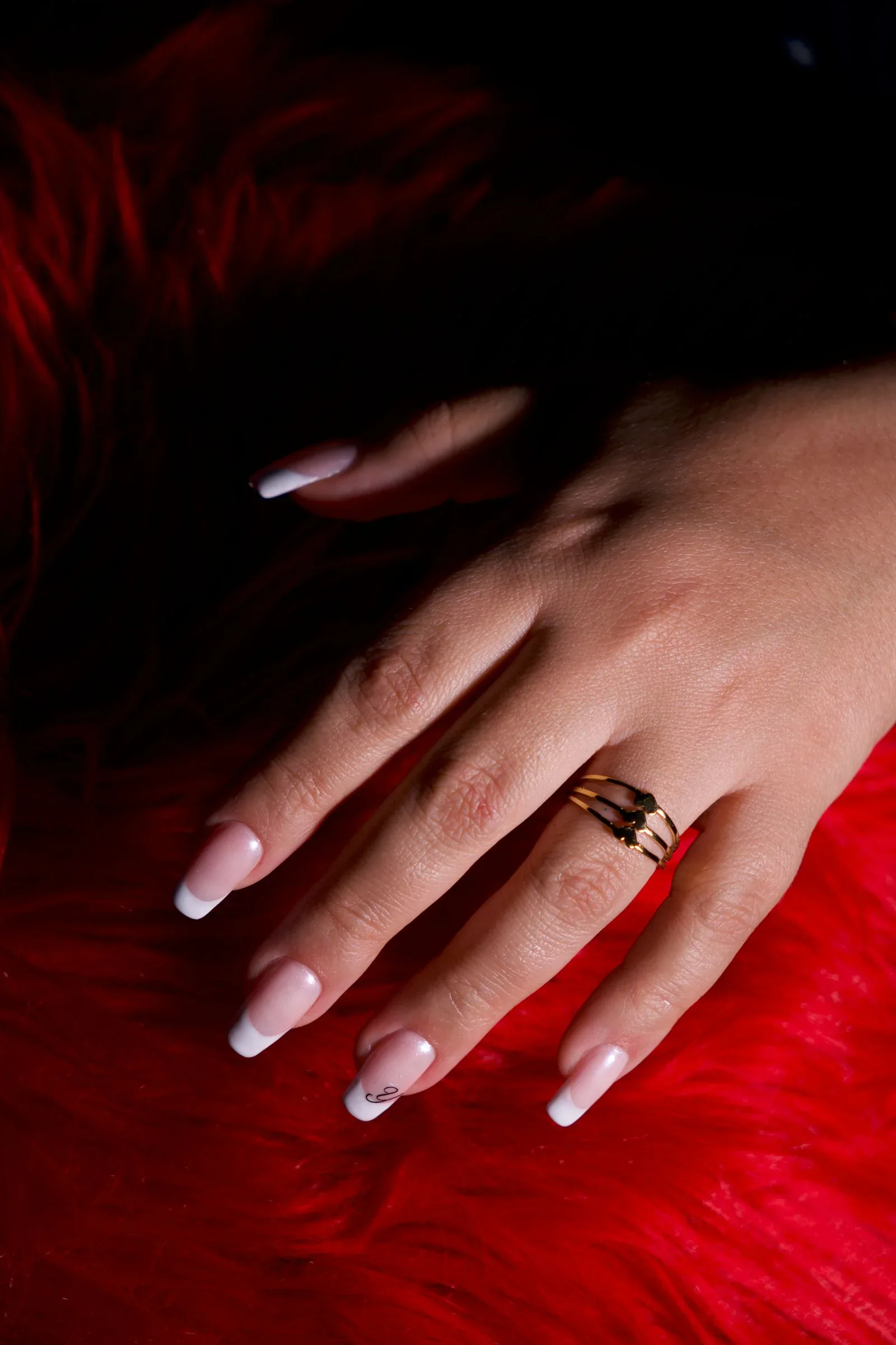Soft white French tips on a pink base, hand resting on red faux fur