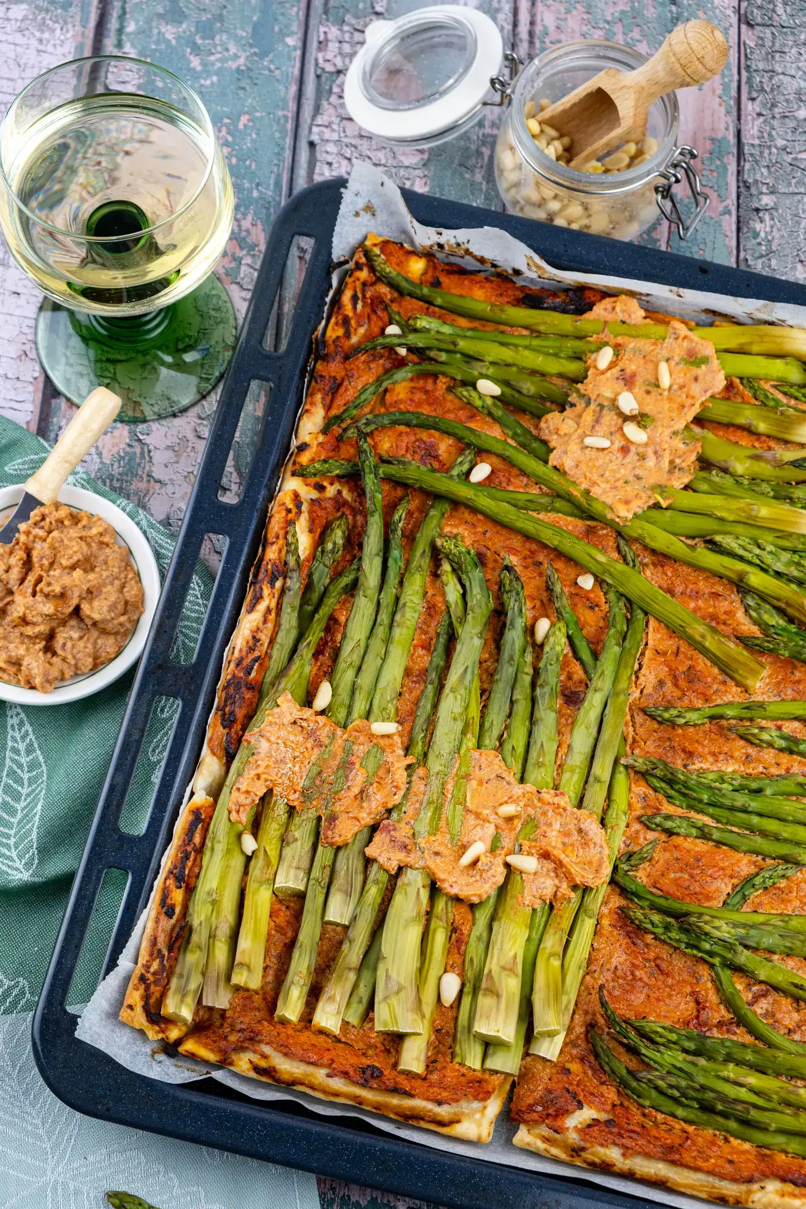 A rectangular asparagus tart with pine nuts on a baking sheet