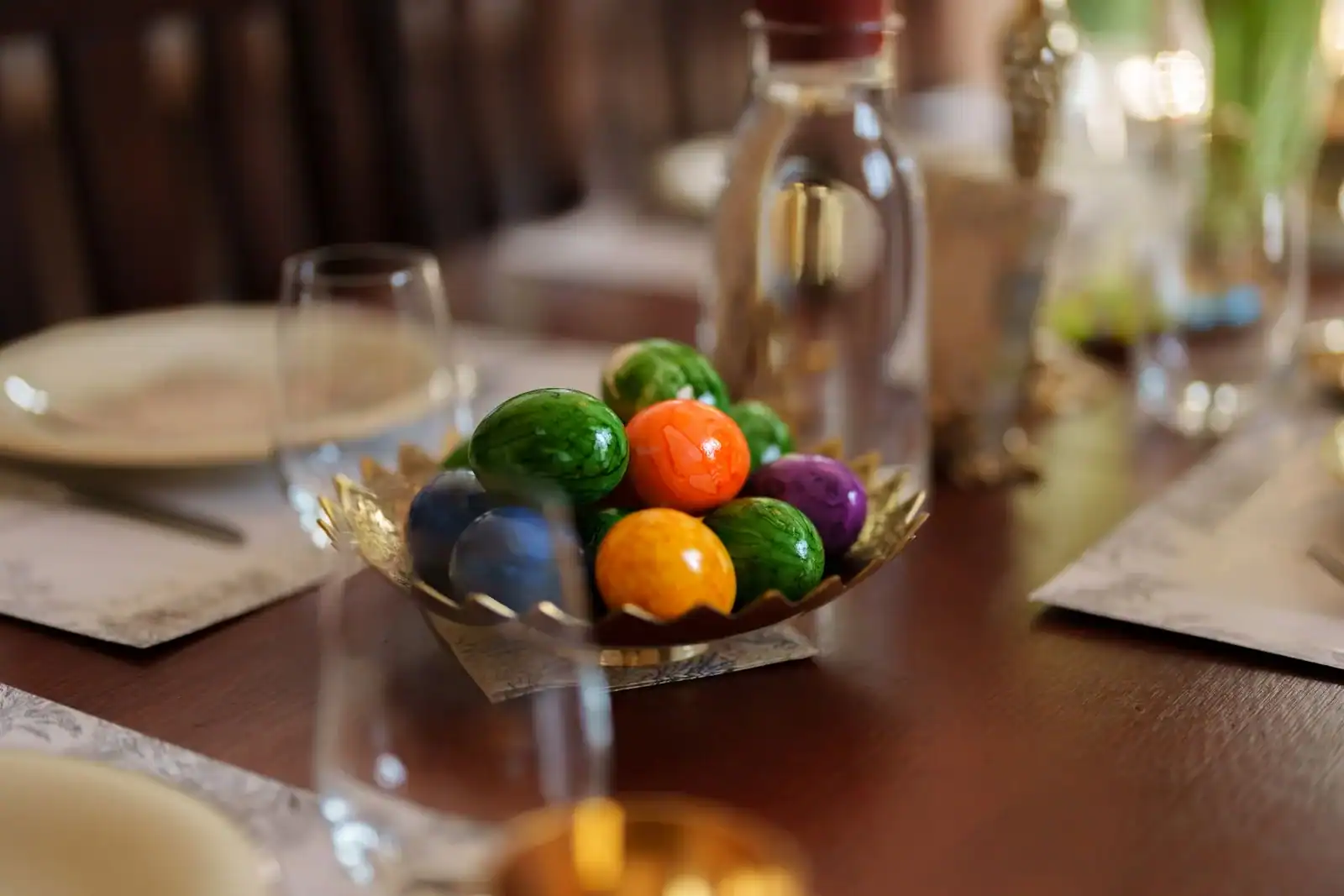 An Easter dining table with a bowl of painted eggs beside wine glasses and place settings