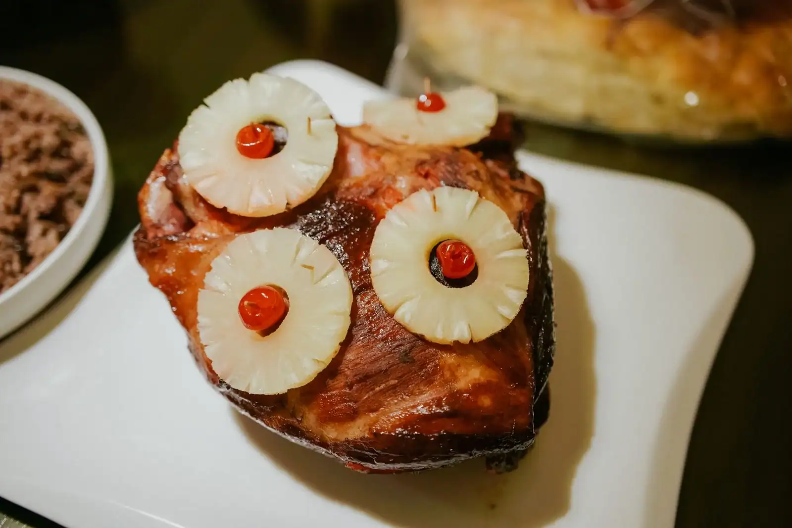 A baked ham topped with pineapple rings and cherries on a white platter