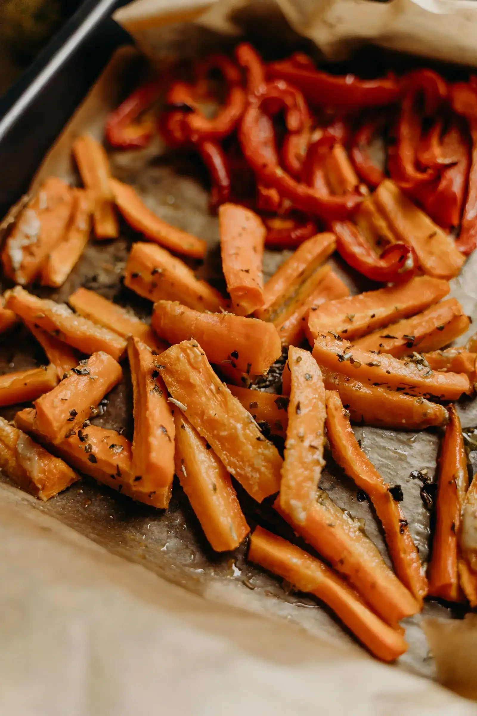 Roasted carrot sticks and red pepper strips with herbs on a lined baking tray