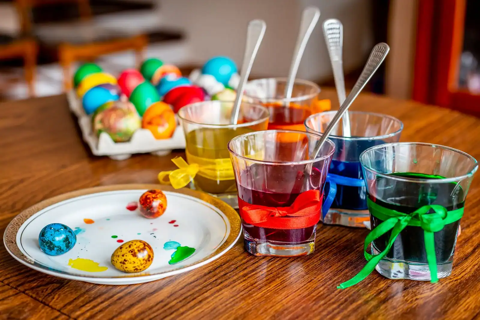 Easter egg decorating ideas: cups of dye, spoons and a carton of eggs on a wooden table
