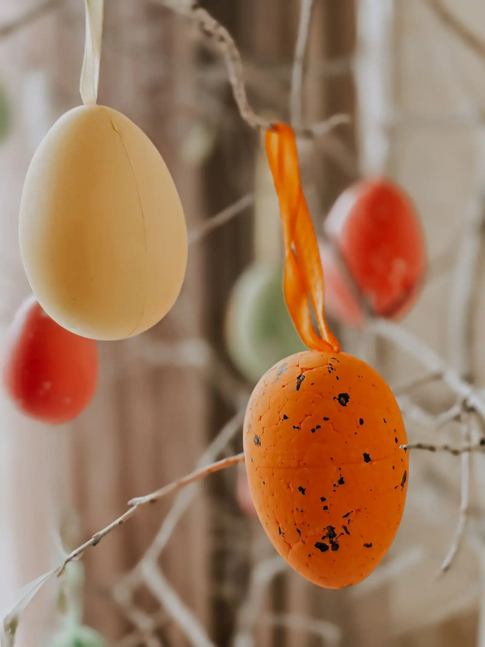 Orange and cream decorated Easter eggs hanging from bare branches on ribbons