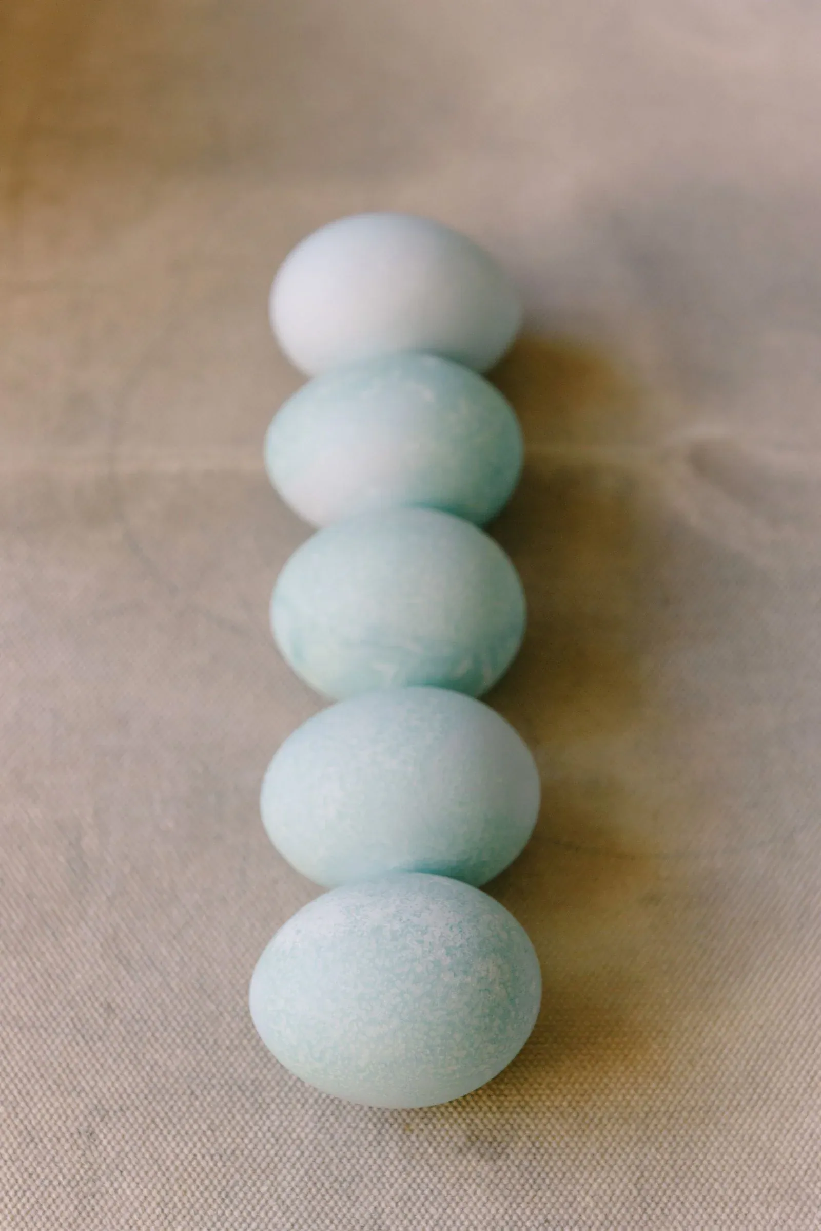 Five pale blue Easter eggs in a vertical row on a linen cloth