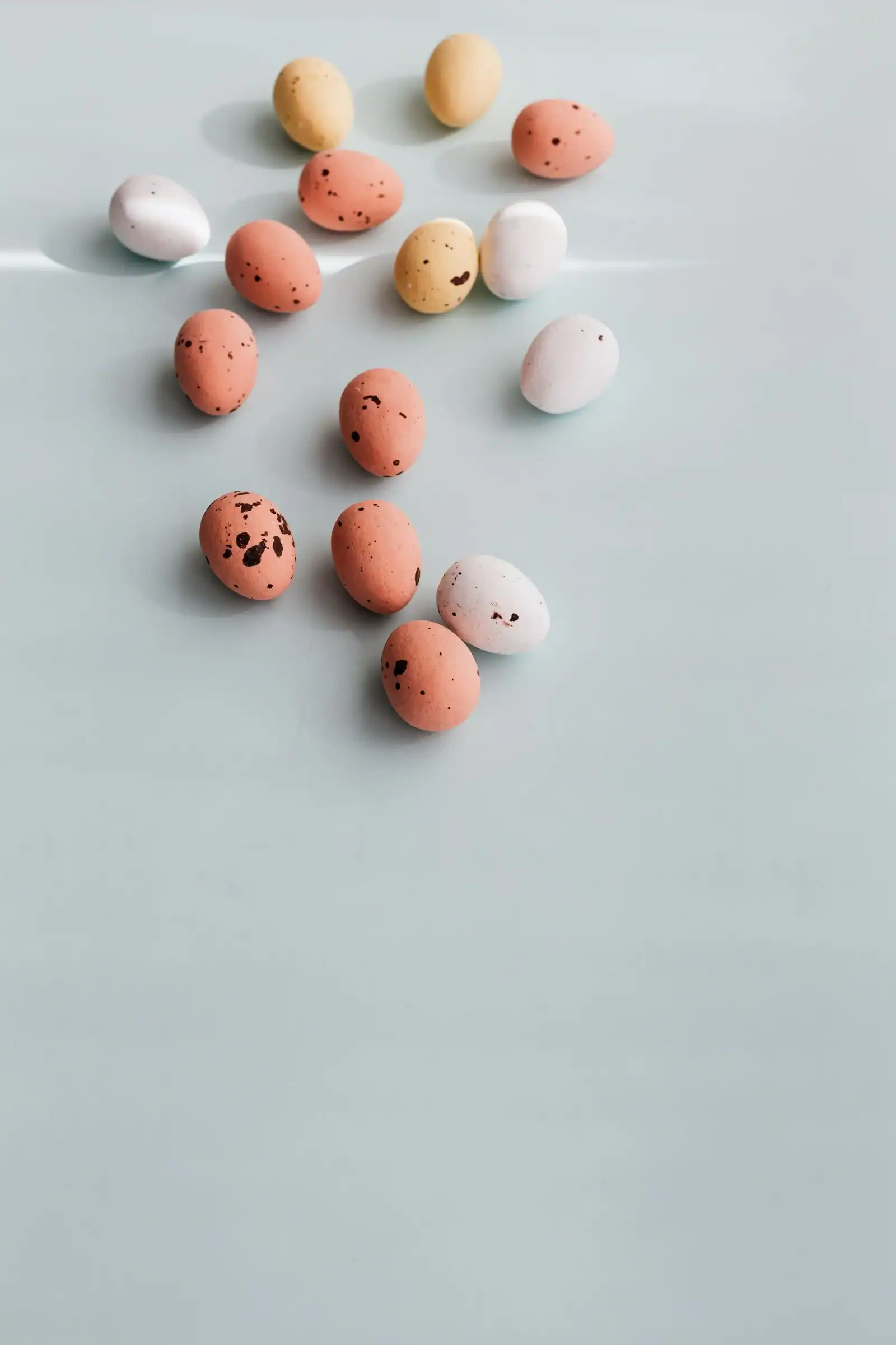 Small pastel Easter eggs with brown speckles scattered on a pale gray surface