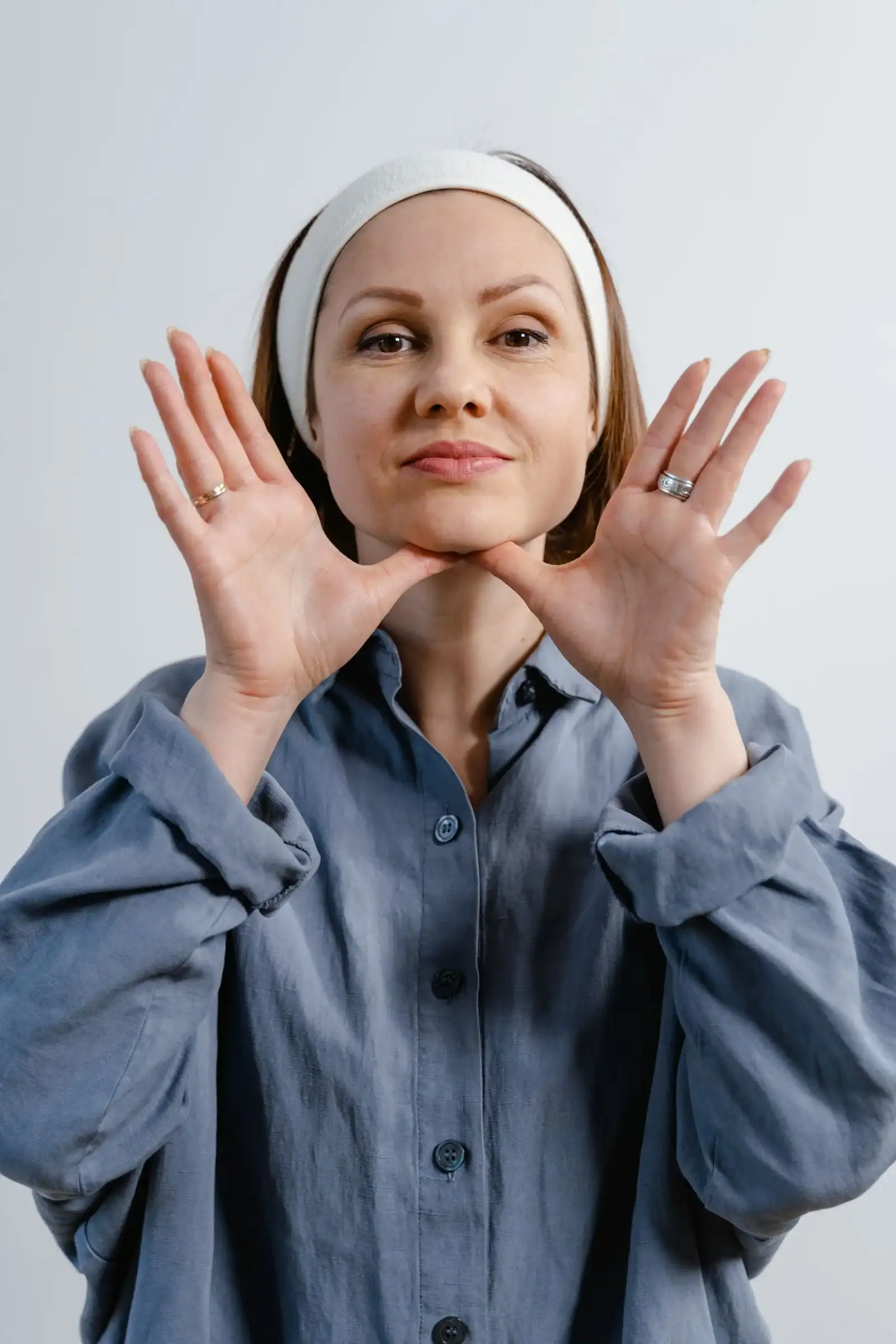 A woman in a headband framing her jaw with both hands for a facial massage