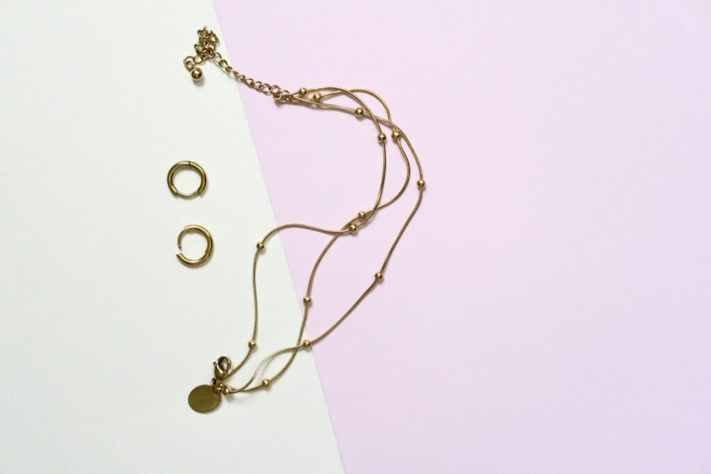 Gold chain necklace and small gold hoop earrings on a pastel background