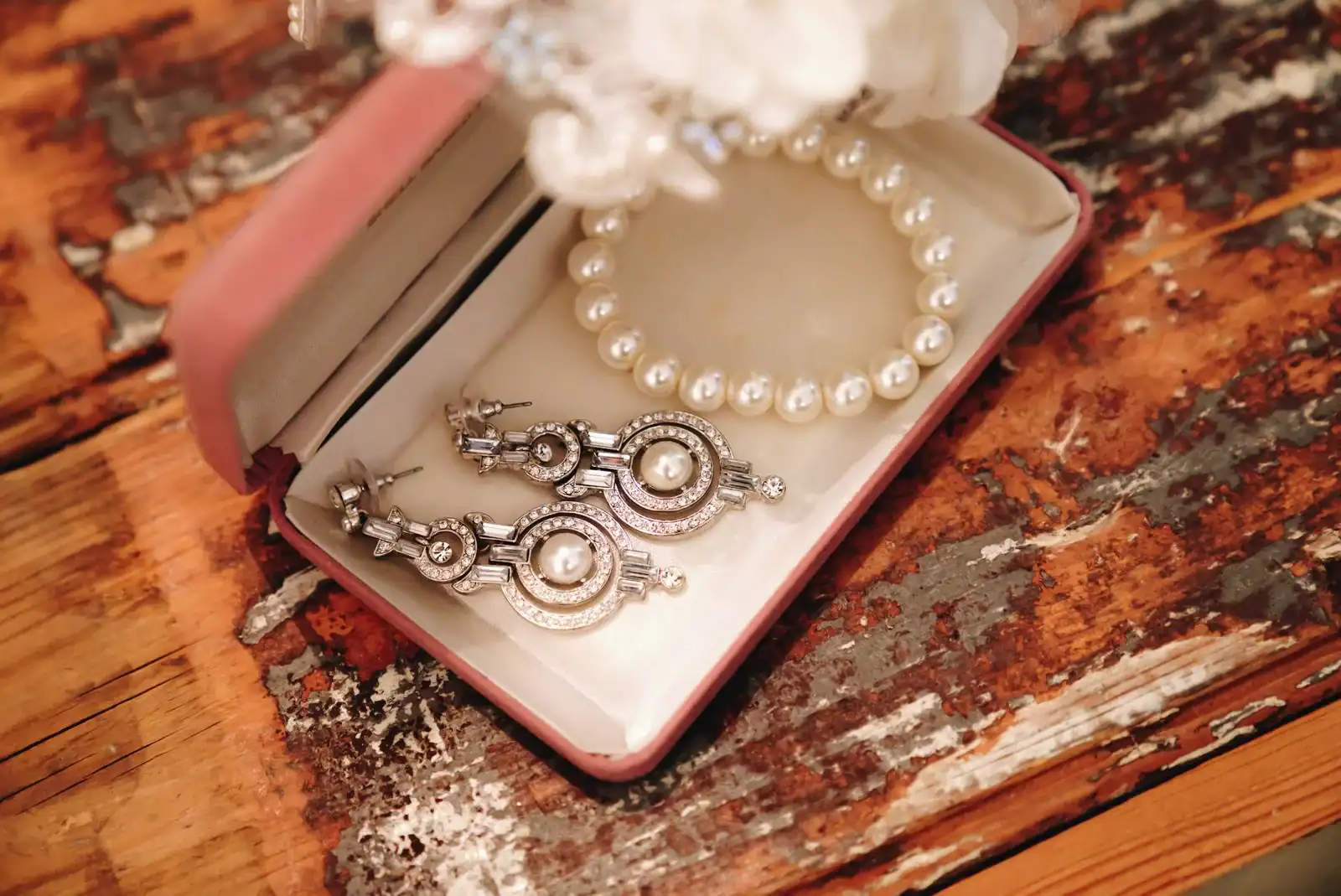 A pearl necklace and crystal drop earrings in an open pink box on a weathered wooden table