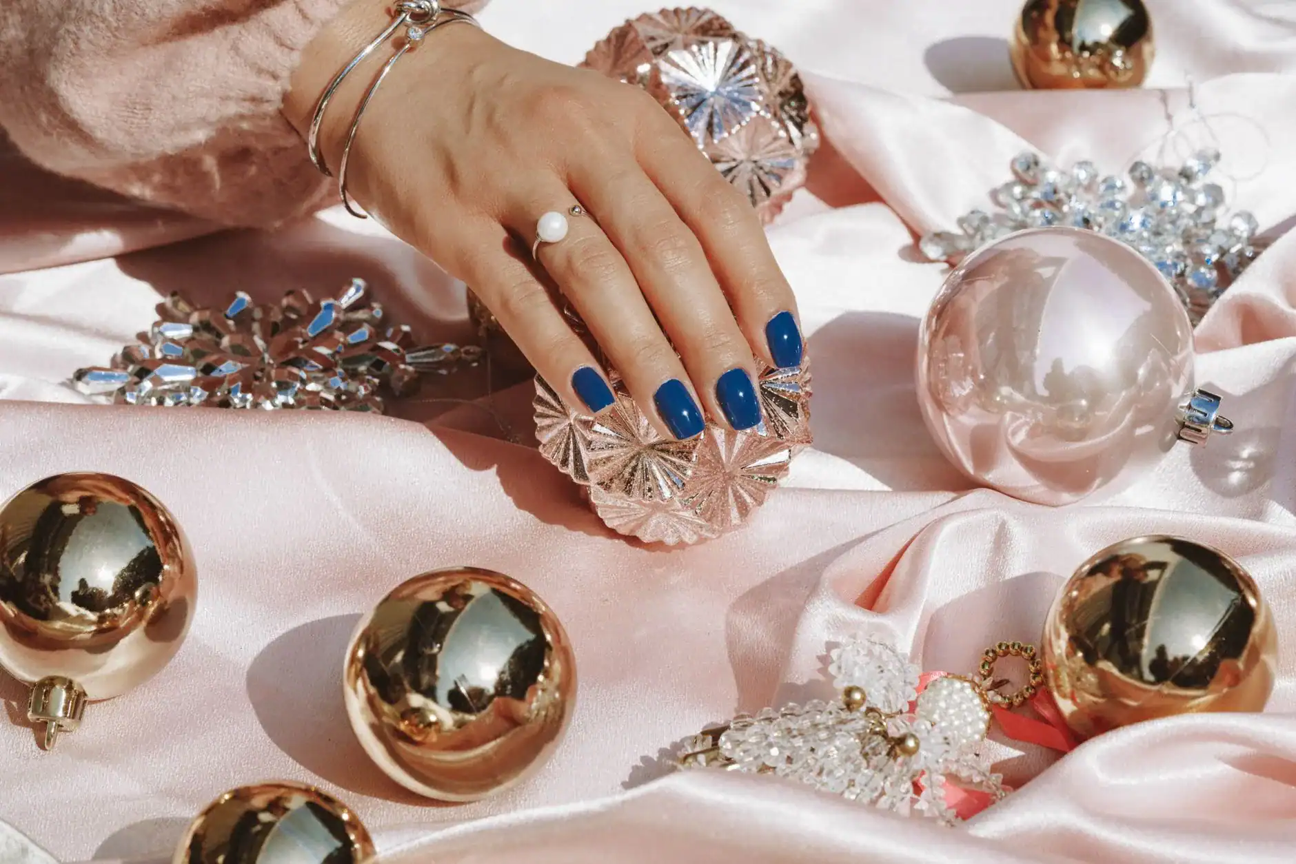 Navy blue manicure resting on pink satin with silver baubles