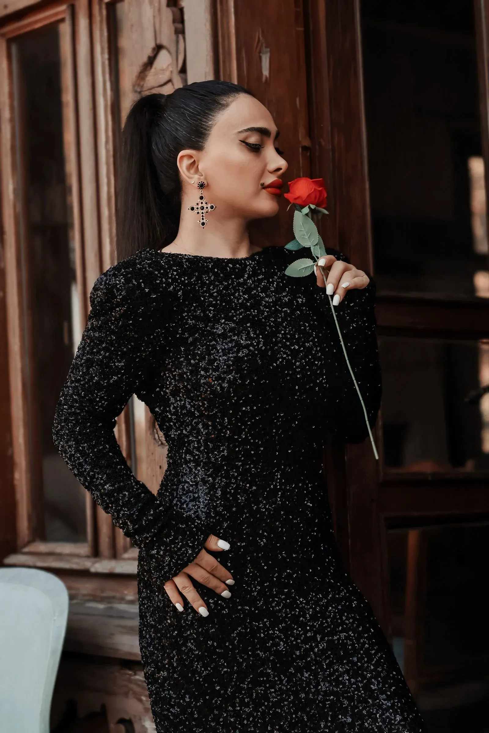 A woman in a long-sleeve black sequin dress holding a red rose