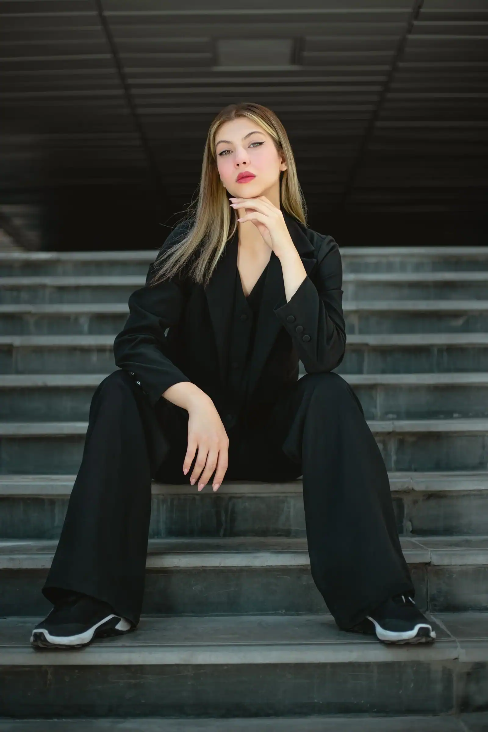 A woman in a black suit with wide trousers sits on stone steps
