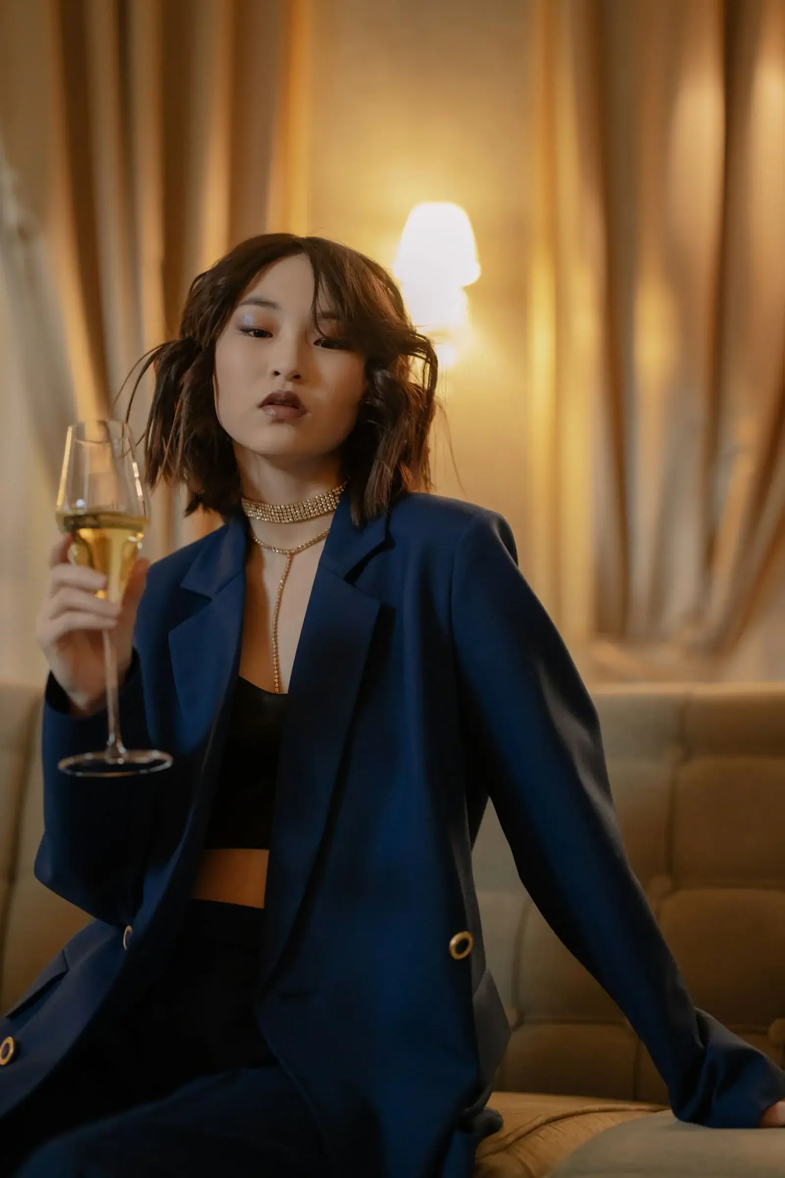 A woman in a navy blazer suit holds a glass of champagne in a warm-lit room