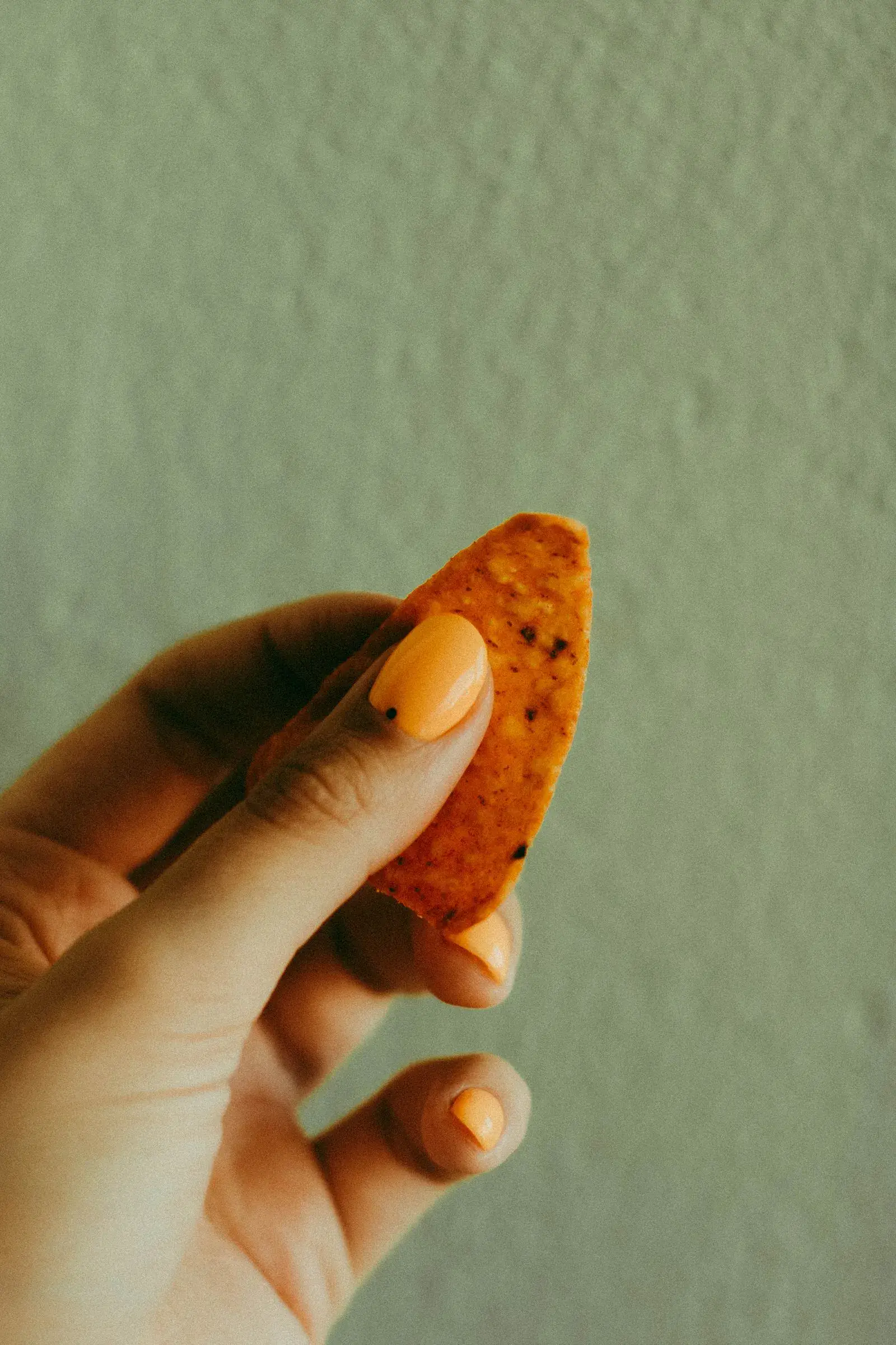 A hand with golden orange nails holding a leaf