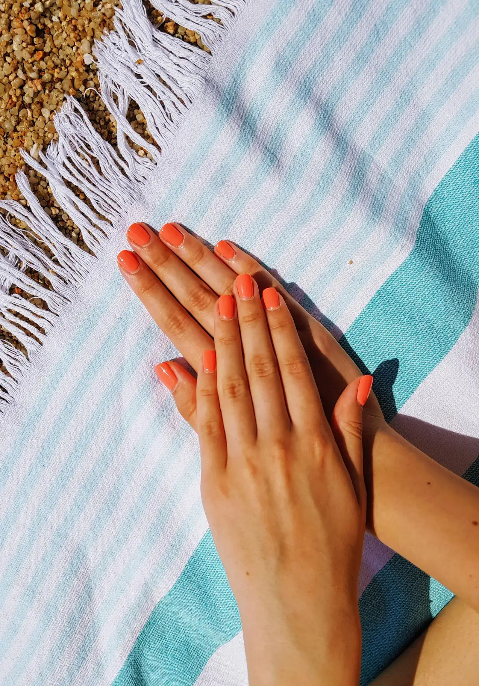 Two hands with coral orange nails on a striped towel