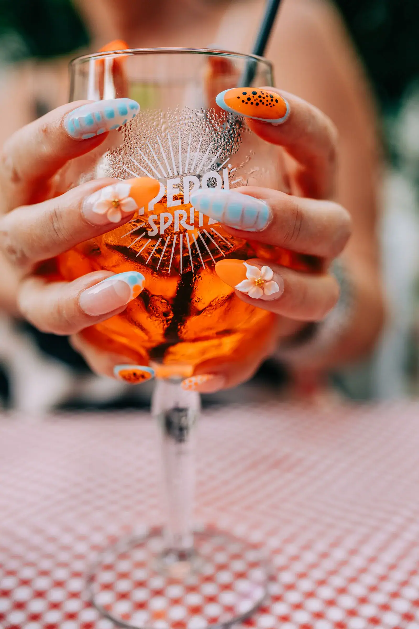 Hands with orange and pale blue nails holding a glass of orange spritz