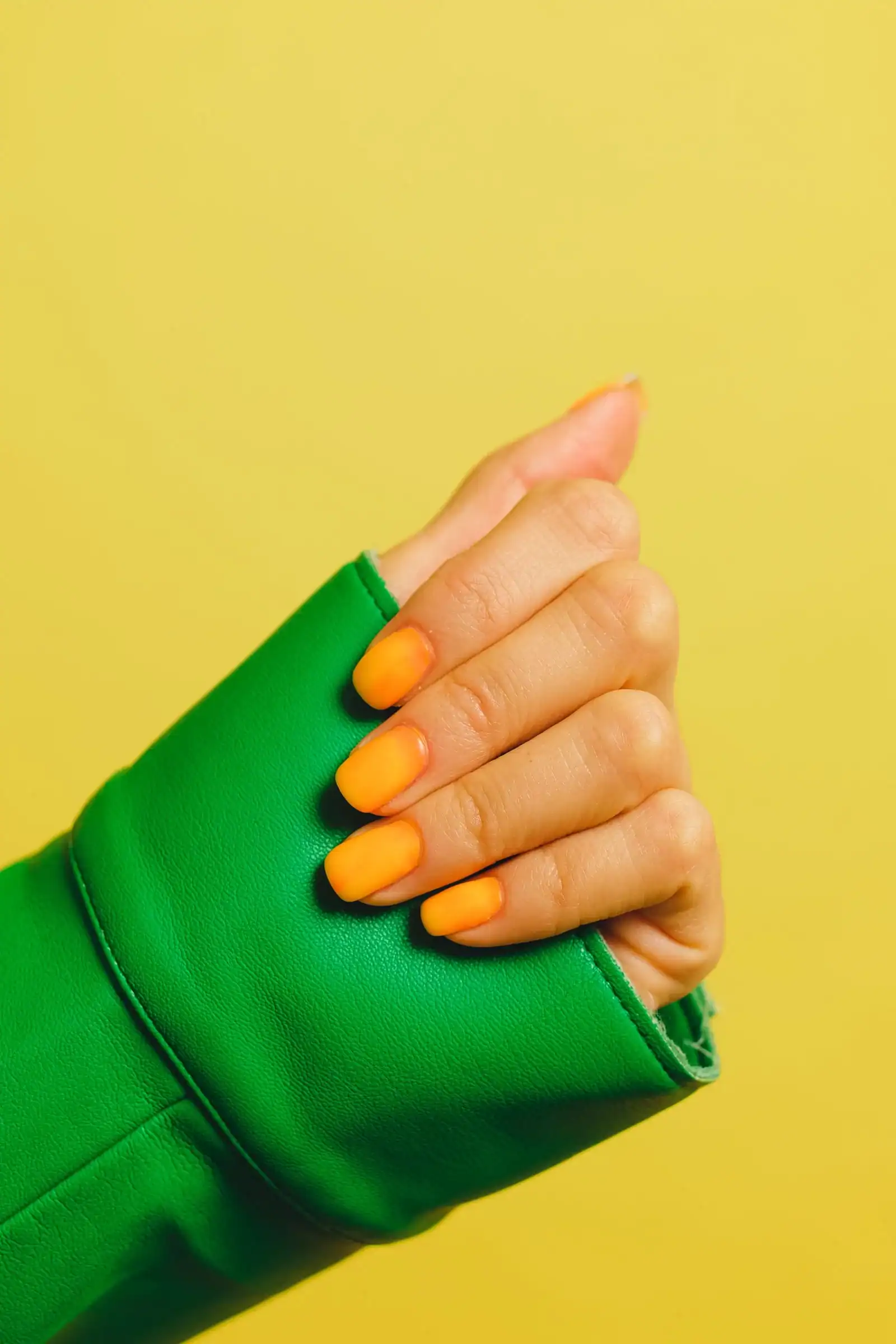 A hand with tangerine orange nails against a yellow background