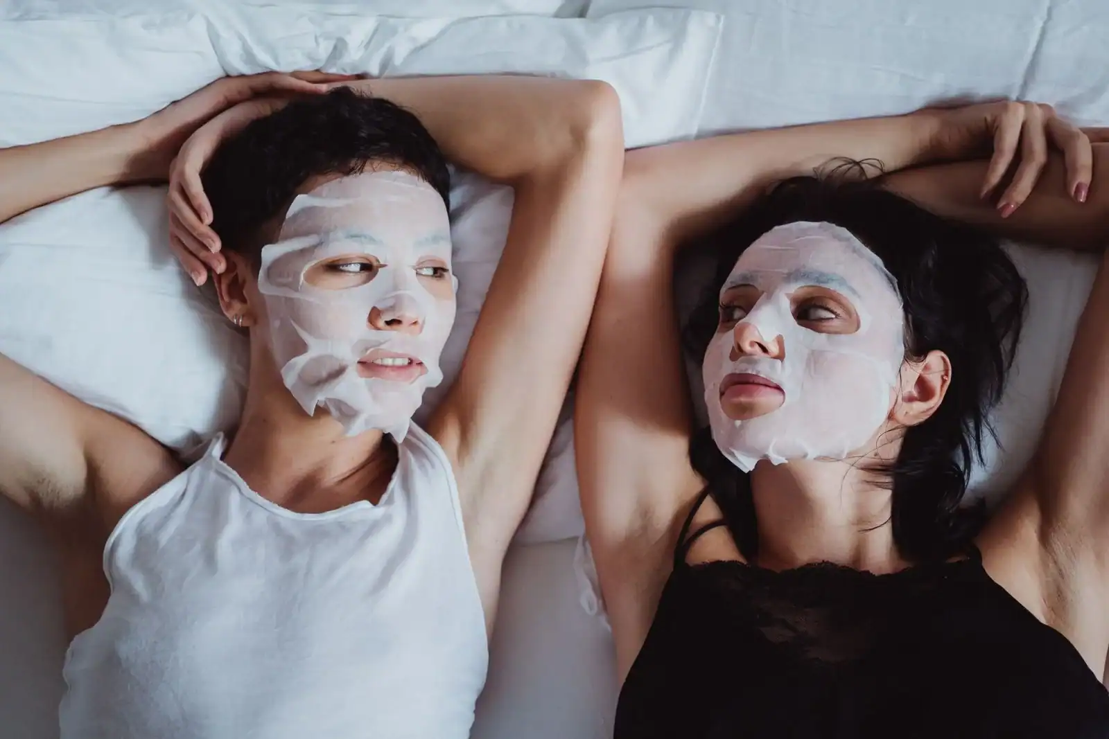 Two friends relaxing in bed with sheet masks