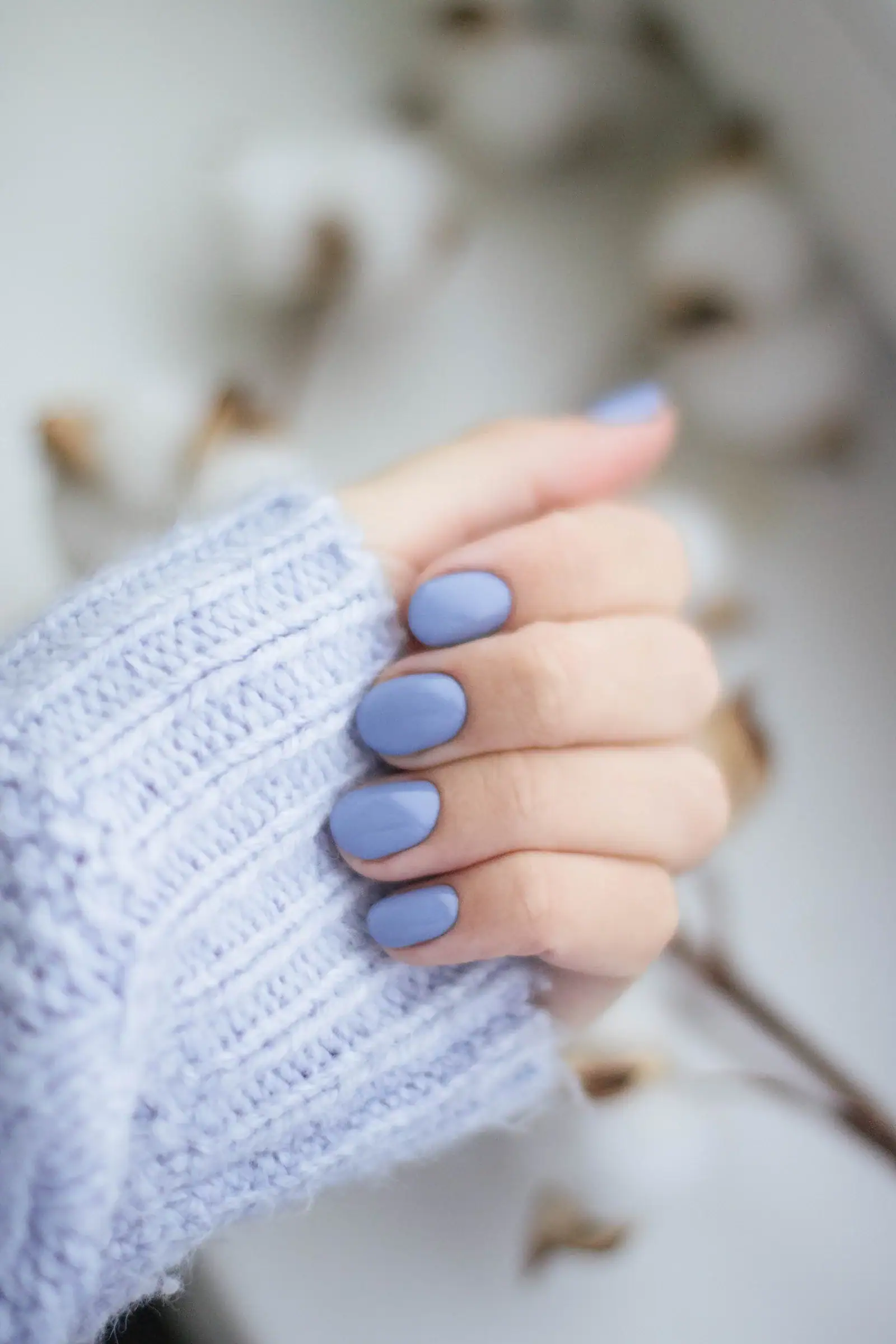 A hand with purple manicured nails resting on a knit sweater.