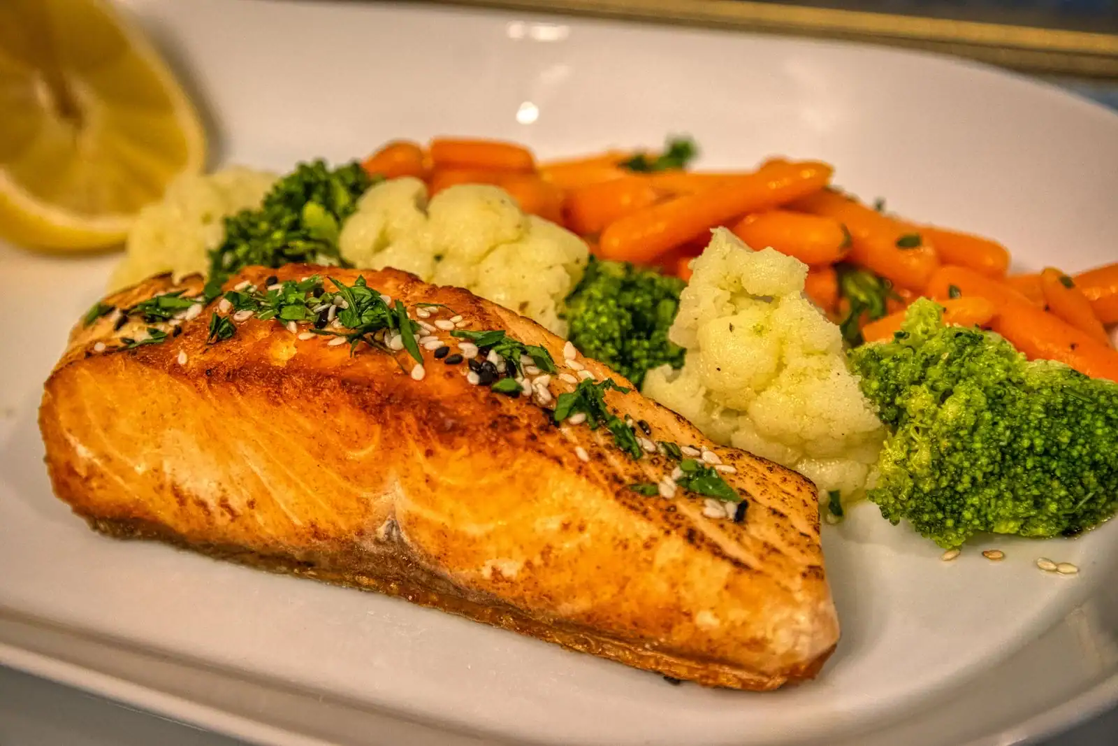 A salmon fillet with broccoli, cauliflower and carrots and a lemon wedge on a plate