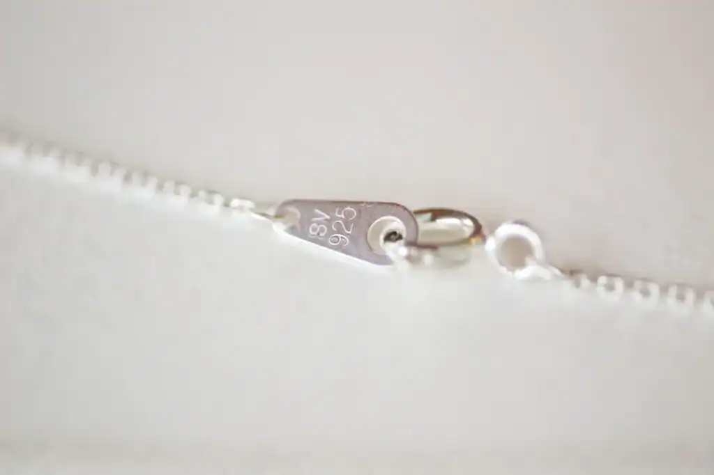 Close-up of a silver chain with a small tag stamped 925 next to the lobster clasp.