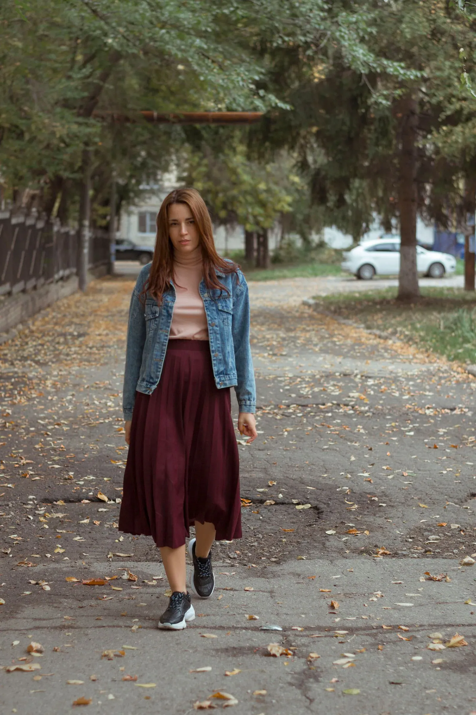 A woman in a denim jacket and a burgundy midi skirt on a park path