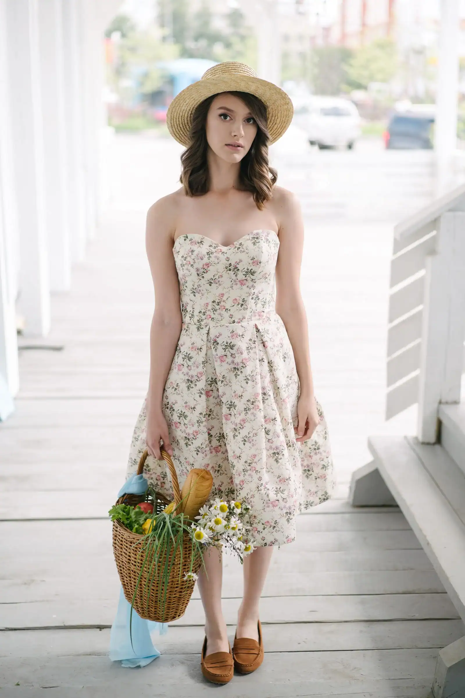 A woman in a floral sundress and a straw hat carrying a basket of flowers