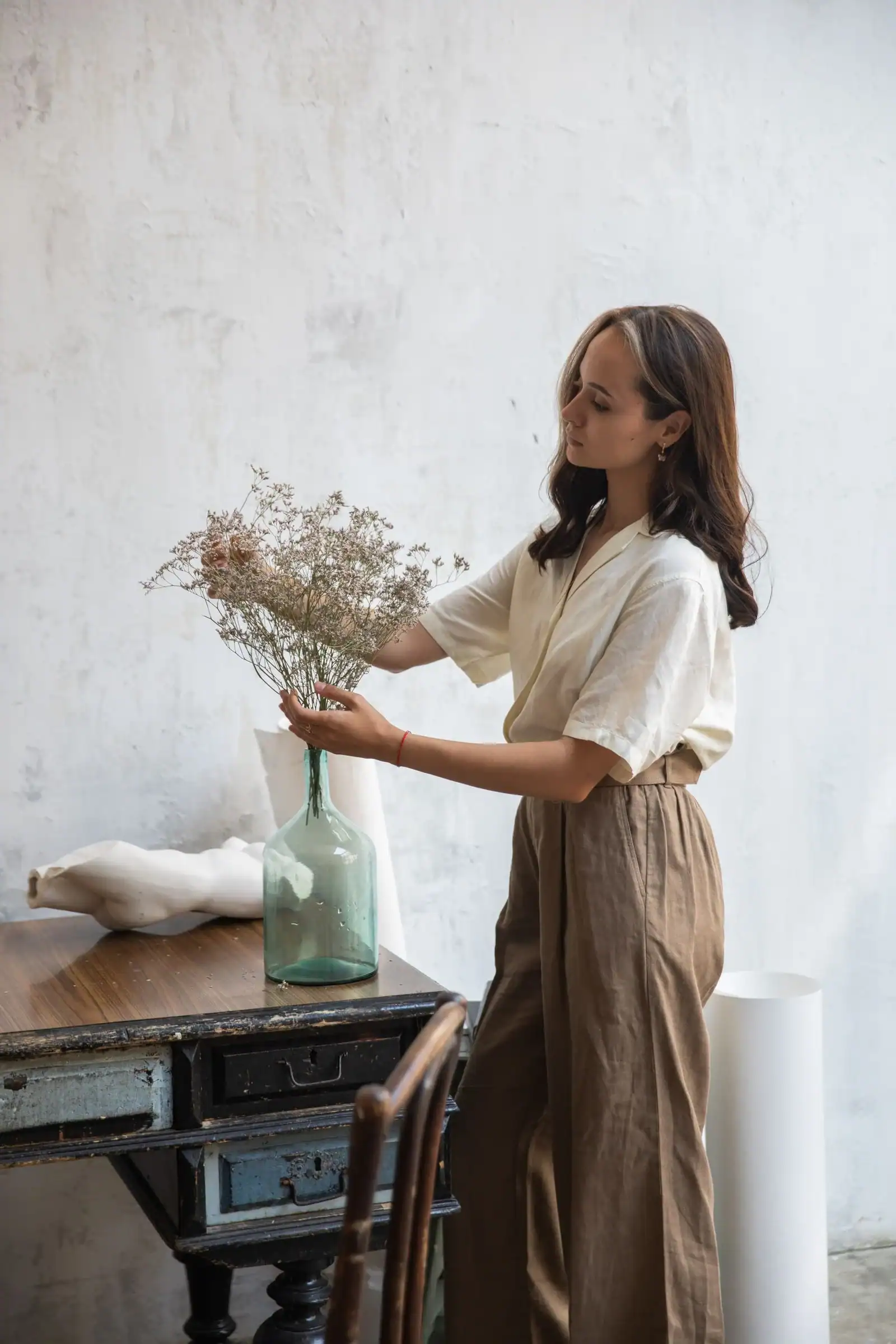 A woman in a white top and wide brown trousers arranging flowers