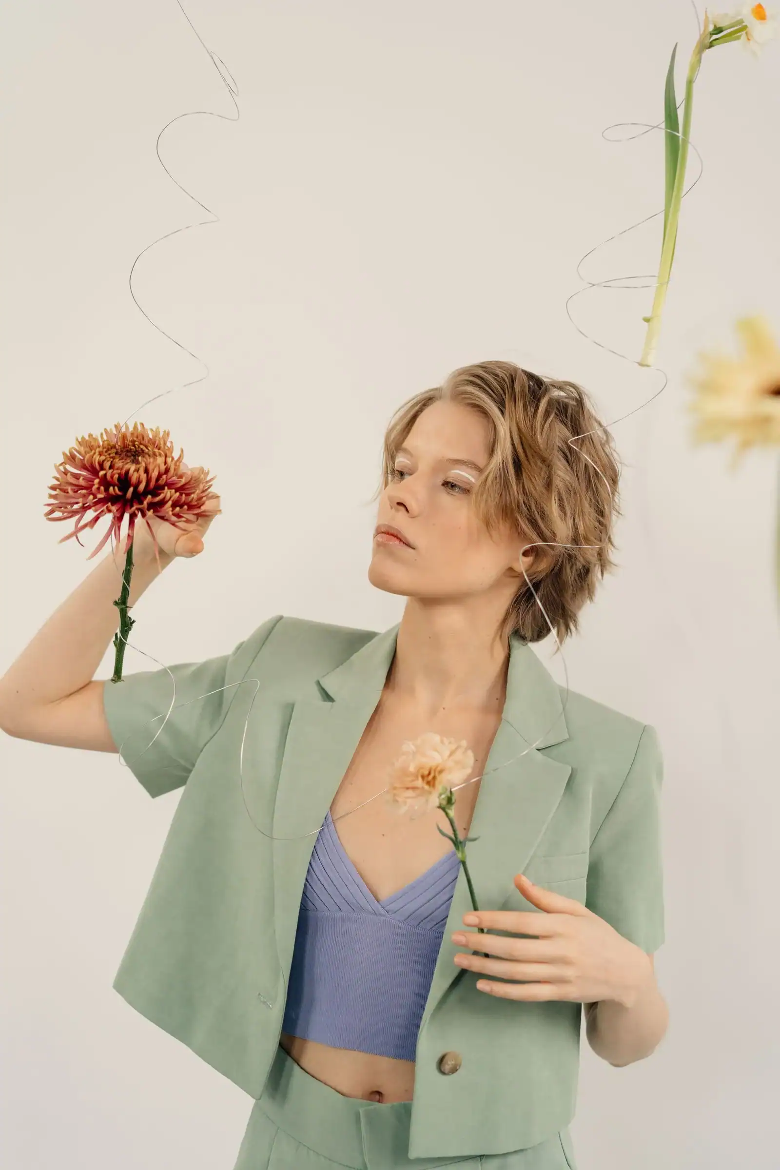 A woman in a sage green blazer and a lavender top holding a red flower