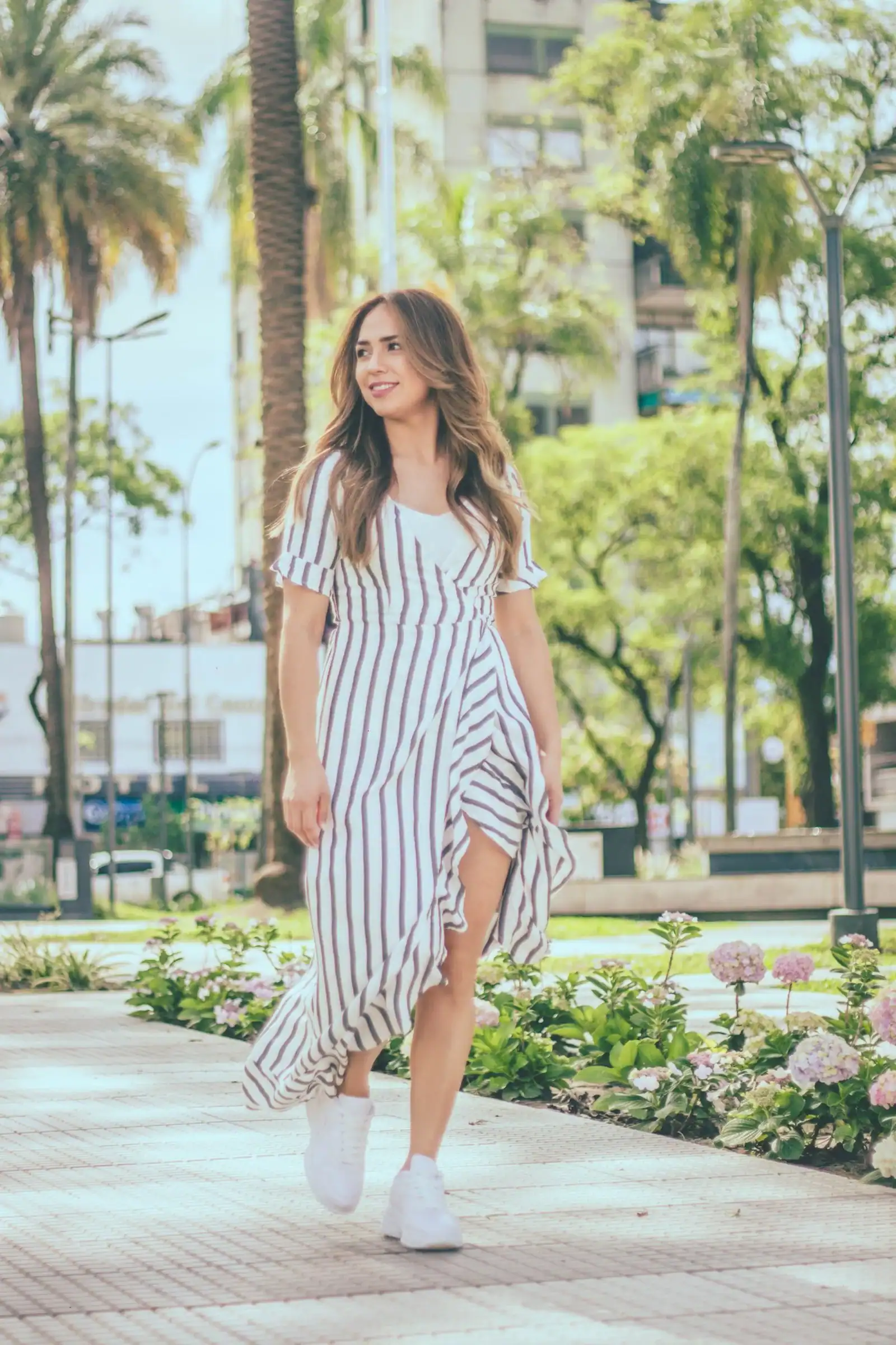 A woman in a striped dress and white sneakers walking in a park