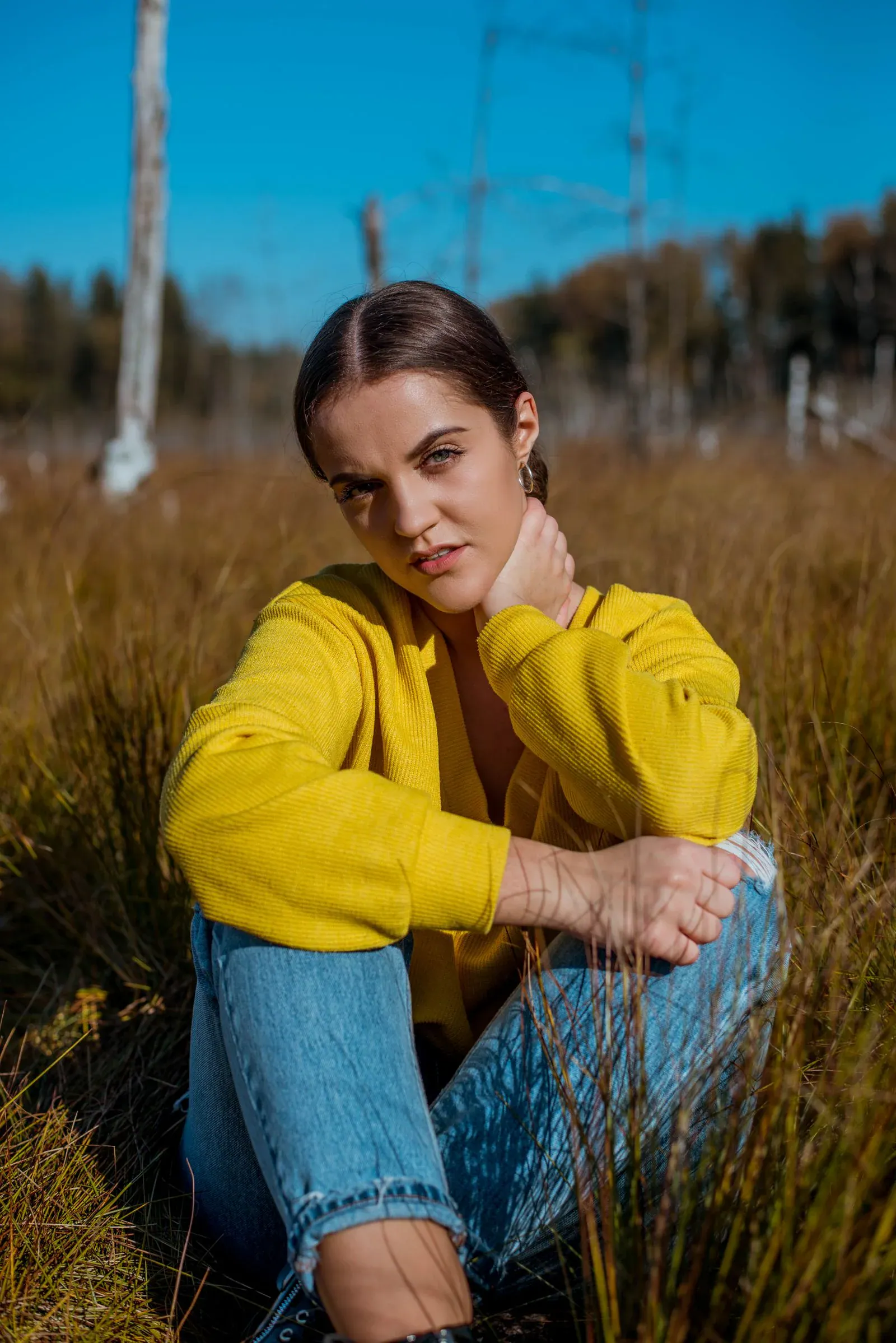 A woman in a yellow sweater and jeans sitting in tall grass