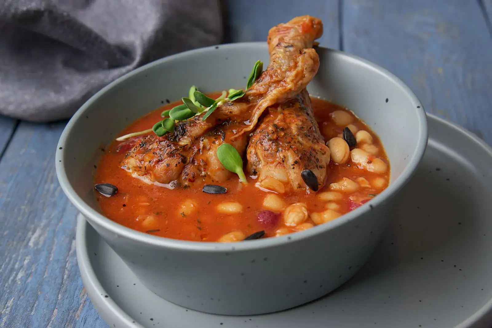 A bowl of tomato stew with chicken pieces and white beans